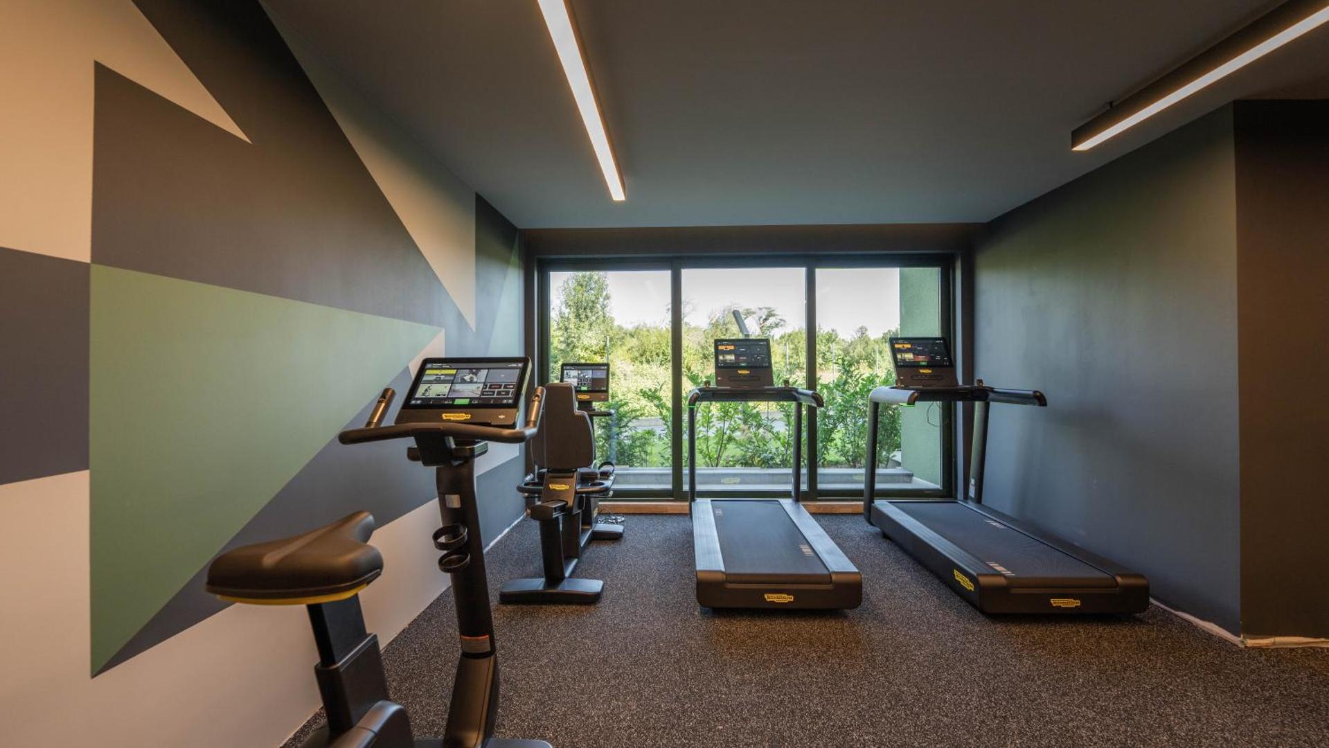 HVD Reina del Mar modernā fitness zāle ar Technogym skrejceliņiem un velotrenažieriem — skats caur logu uz zaļo zonu