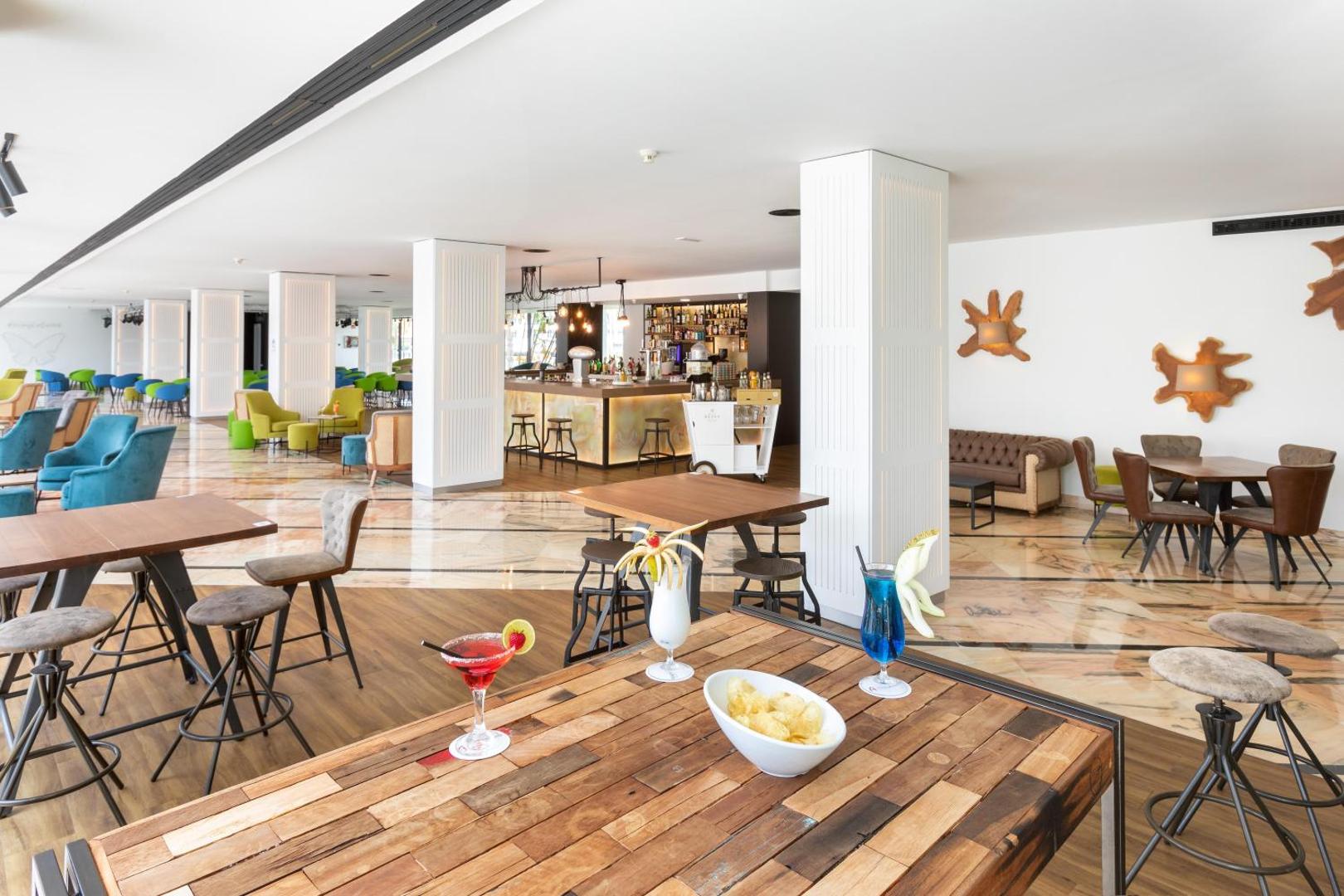 Alexandre Hotel La Siesta plašā atpūtas zona ar bāra leti, galdiņiem un krāsainām mēbelēm gaišā, modernā interjerā Kanāriju salās.
