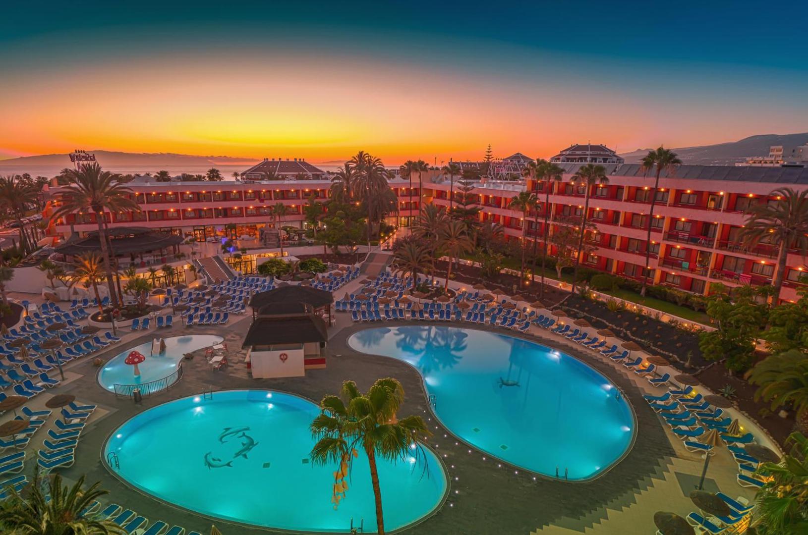 Alexandre Hotel La Siesta viesnīcas komplekss un izgaismoti baseini saulrieta laikā Playa de las Americas, Tenerifē
