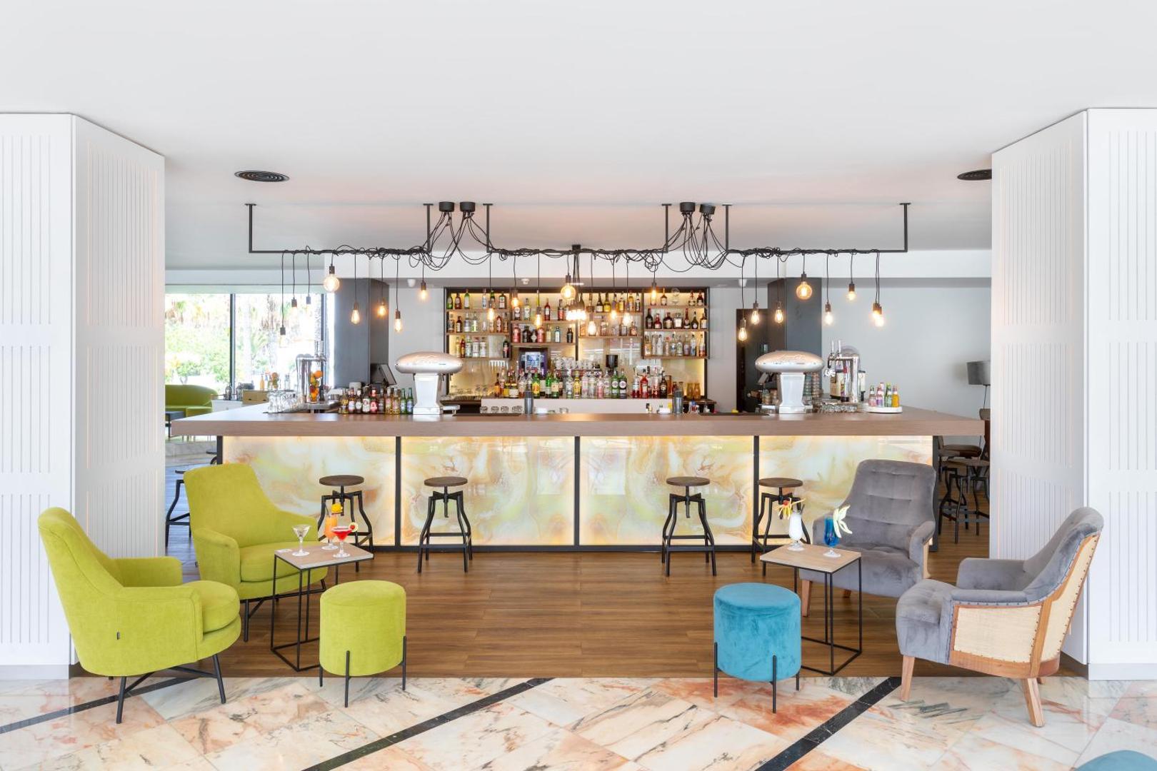 Alexandre Hotel La Siesta modernais lobby bārs Tenerifē ar krāsainiem atpūtas krēsliem, dizaina apgaismojumu un plašu dzērienu izvēli pie letes.