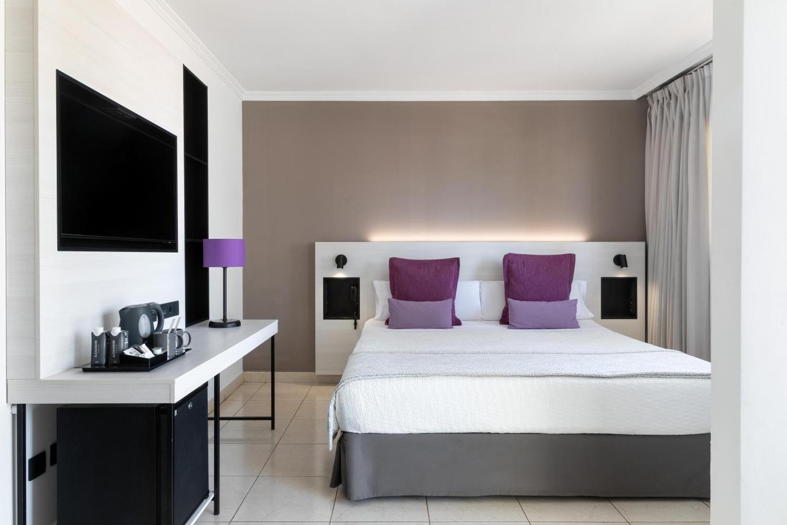 Alexandre Hotel La Siesta moderns divvietīgs numurs ar violetiem akcentiem, lielu gultu, sienas televizoru un kafijas pagatavošanas stūrīti