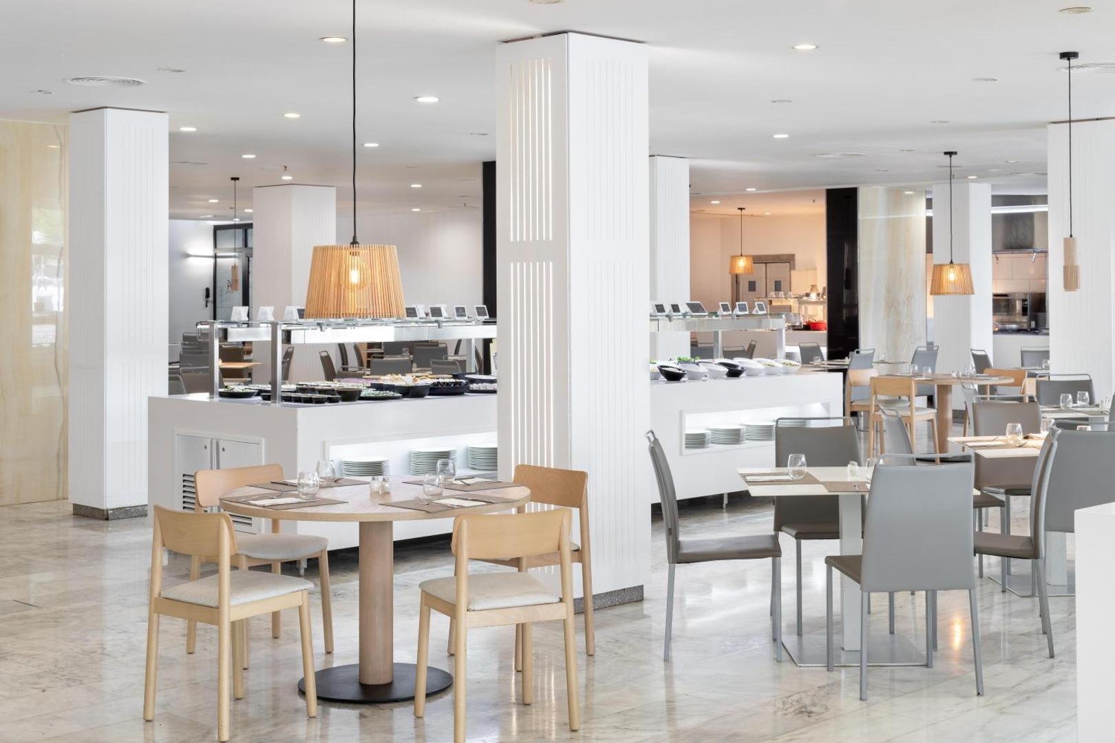 Alexandre Hotel La Siesta gaišā un modernā restorāna zāle ar koka galdiem, pelēkiem krēsliem un bufetes letēm