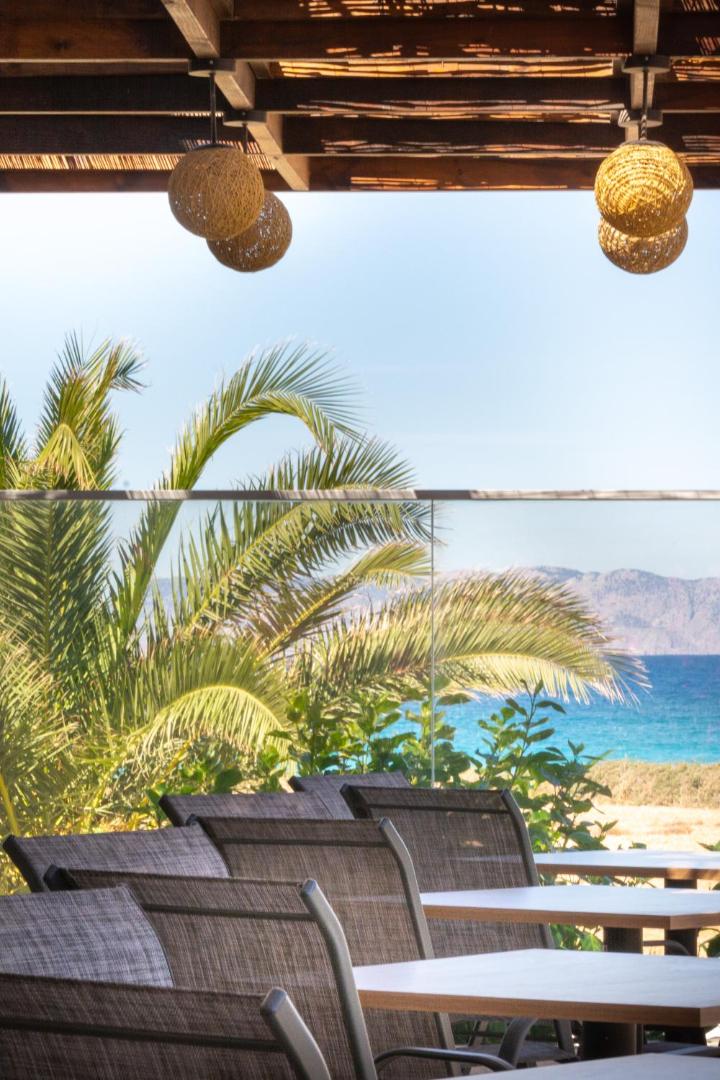 Nirvana Beach Hotel restorāna āra terase ar moderniem krēsliem, dekoratīvām lampām un skatu uz palmu un jūru