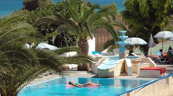 Nirvana Beach Hotel baseina zona ar dekoratīvu strūklaku, palmām un atpūtnieku uz piepūšamā matrača saulainā dienā Rodā