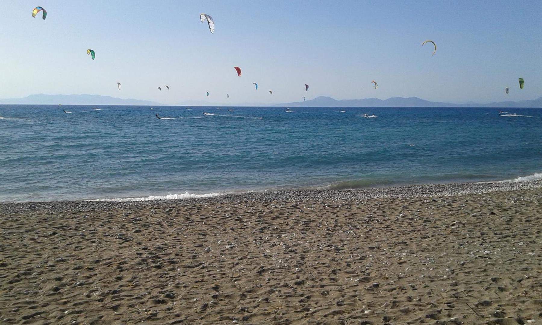 Nirvana Beach Hotel pludmale Rodas salā ar daudziem kaitbordistiem jūrā — skats uz zilo Egejas jūru un tālajiem kalniem