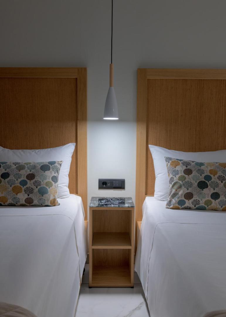 Nirvana Beach Hotel numura interjera detaļa ar divām gultām, koka galvgaliem, modernu lampu un marmora naktsskapīti.