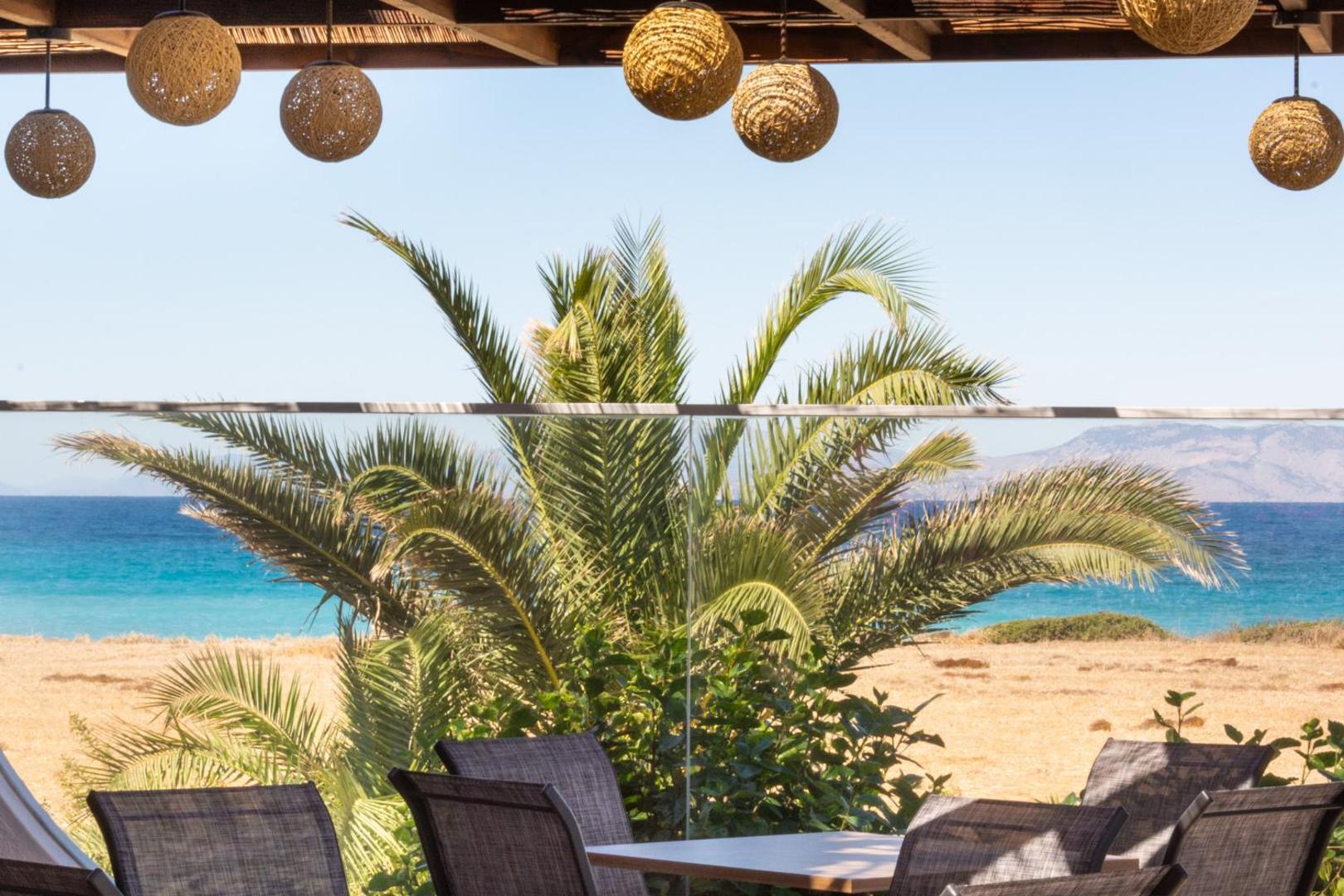 Nirvana Beach Hotel āra terase ar pītiem gaismas ķermeņiem, palmām un skatu uz zilo jūru Rodas piekrastē