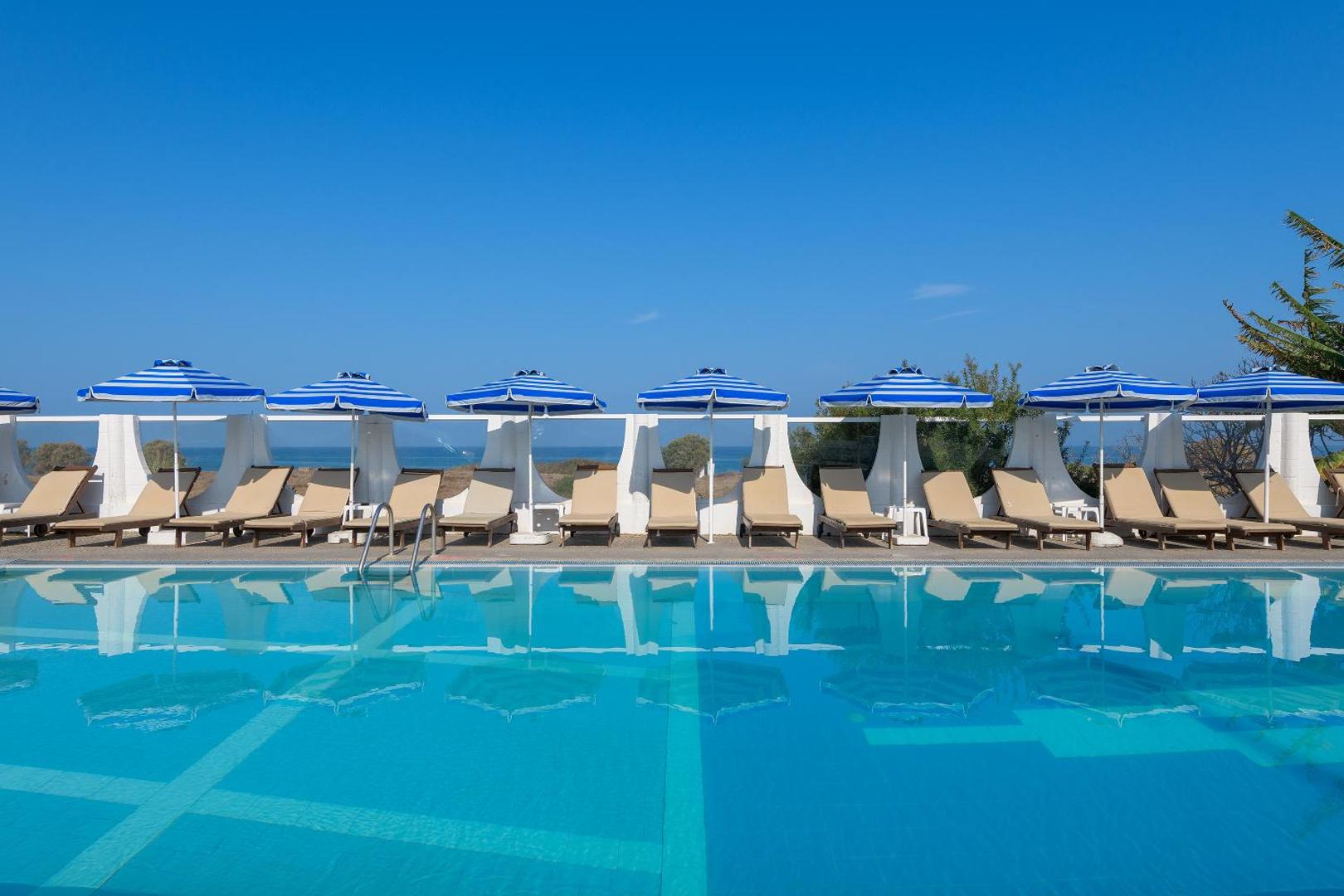 Nirvana Beach Hotel baseina zona ar zili svītrainiem saulessargiem un ērtiem zviļņiem zem skaidrām debesīm.