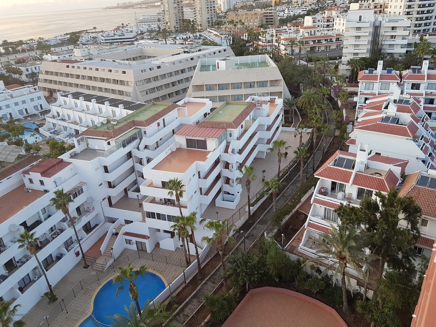 Skats no augšas uz Kn Columbus Aparthotel teritoriju un apkārtējiem bungalo, nelielu baseinu un piekrastes apbūvi Tenerifē saulrietā