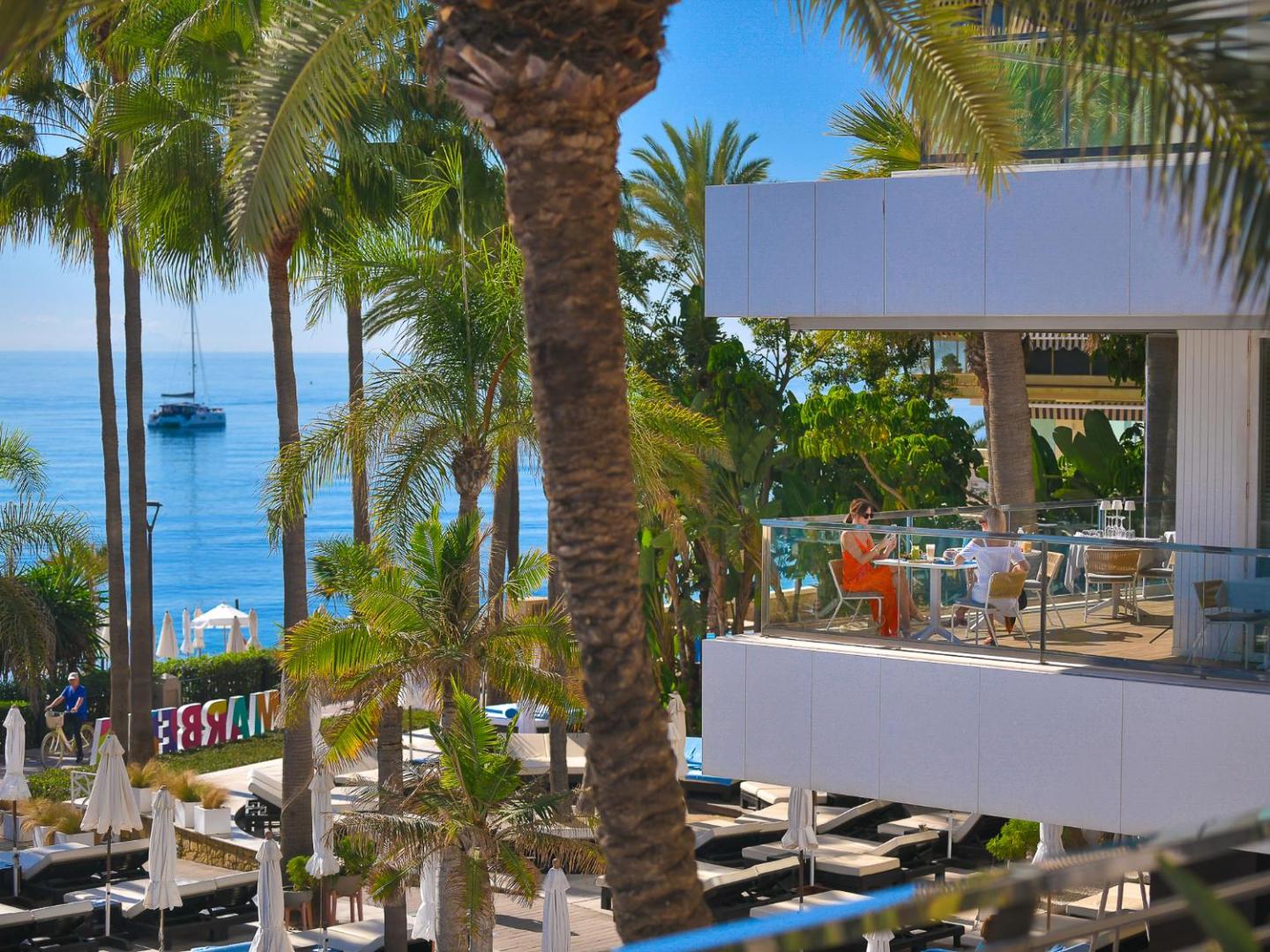 Skats no Amare Beach Hotel Marbella balkona uz palmu dārzu un Vidusjūru ar jahtu tālumā