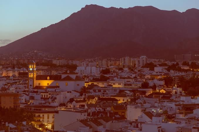 Marbeljas vecpilsētas skats vakarā ar izgaismotu baznīcas torni un kalnu fonā pie Amare Beach Hotel Marbella