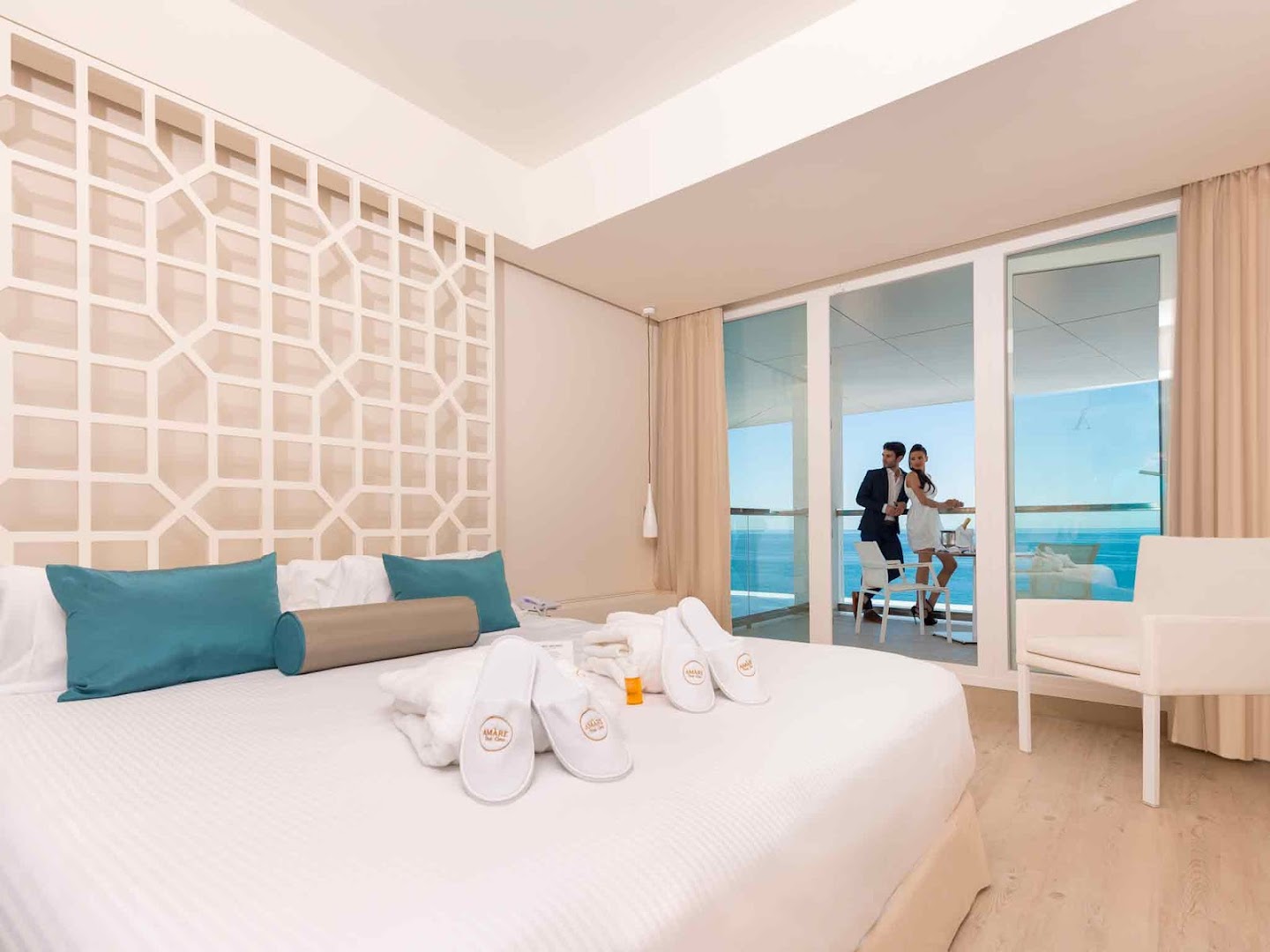 Amare Beach Hotel Marbella luksusa numurs ar lielu gultu, halātiem un pāri uz balkona Marbeljas piekrastē