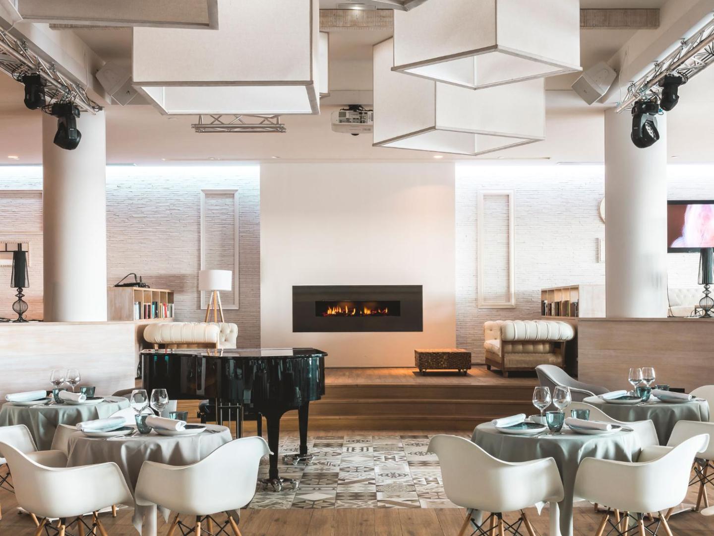 Amare Beach Hotel Marbella restorāna interjers ar klavierēm, modernu kamīnu un eleganti klātiem galdiem vakariņām.