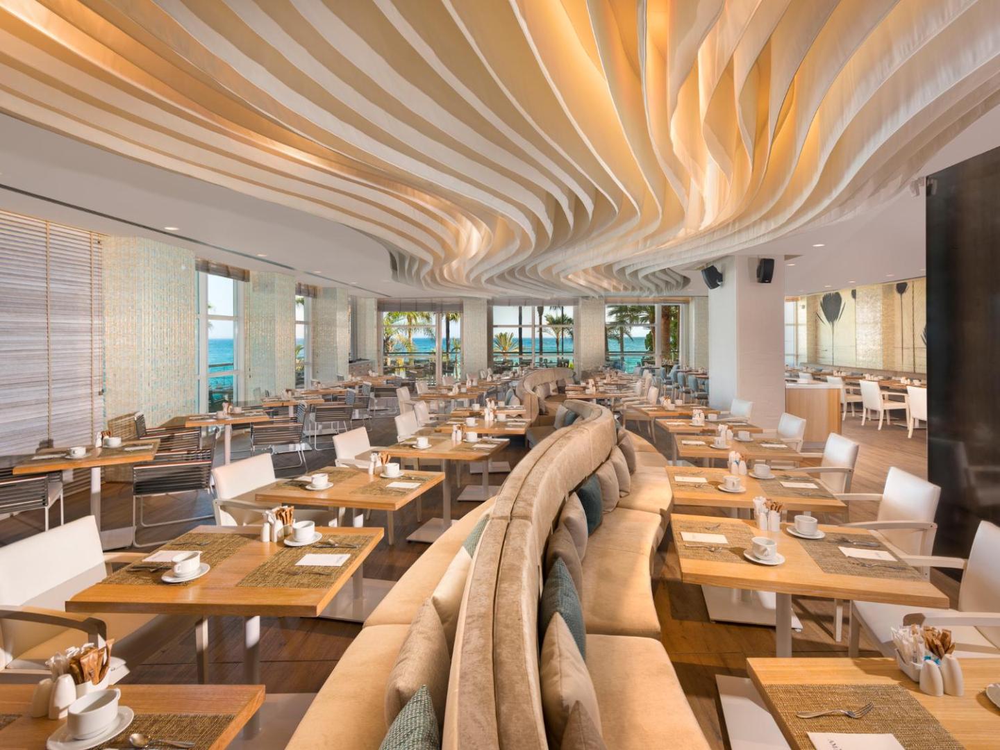 Amare Beach Hotel Marbella plašā brokastu zāle ar modernu griestu dizainu, gaišām mēbelēm un skatu uz jūru caur logiem.