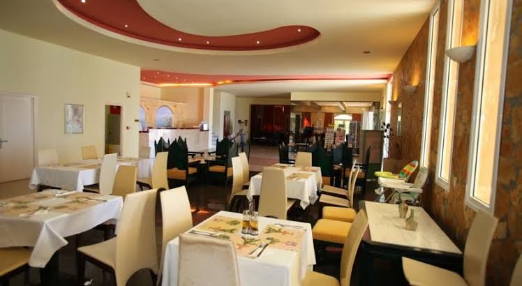 Almyros Beach Resort & Spa galvenais restorāns Korfu salā — plaša telpa ar klātiem galdiem, baltiem galdautiem un krēsliem gaišos toņos