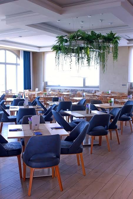 Almyros Beach Resort & Spa restorāna interjers ar modernām mēbelēm, ziliem krēsliem un unikālu griestu dekoru no zaļiem augiem