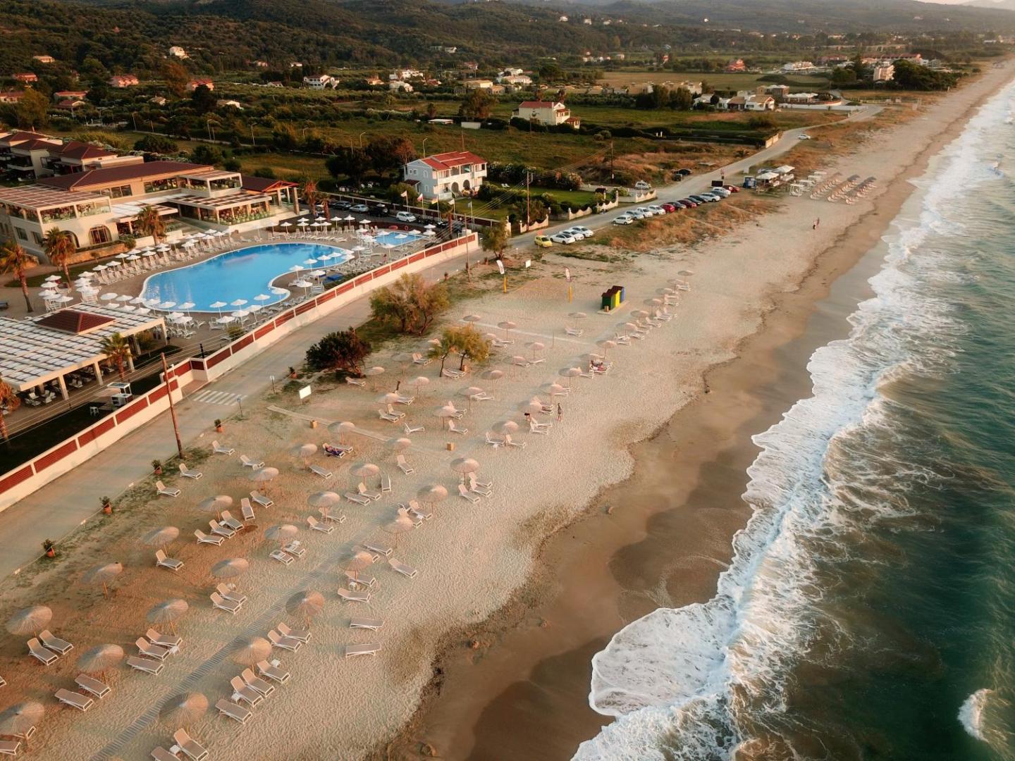 Almyros Beach Resort & Spa panorāmas skats uz viesnīcas teritoriju, lielo āra baseinu un pieguļošo smilšu pludmali Korfu ziemeļos
