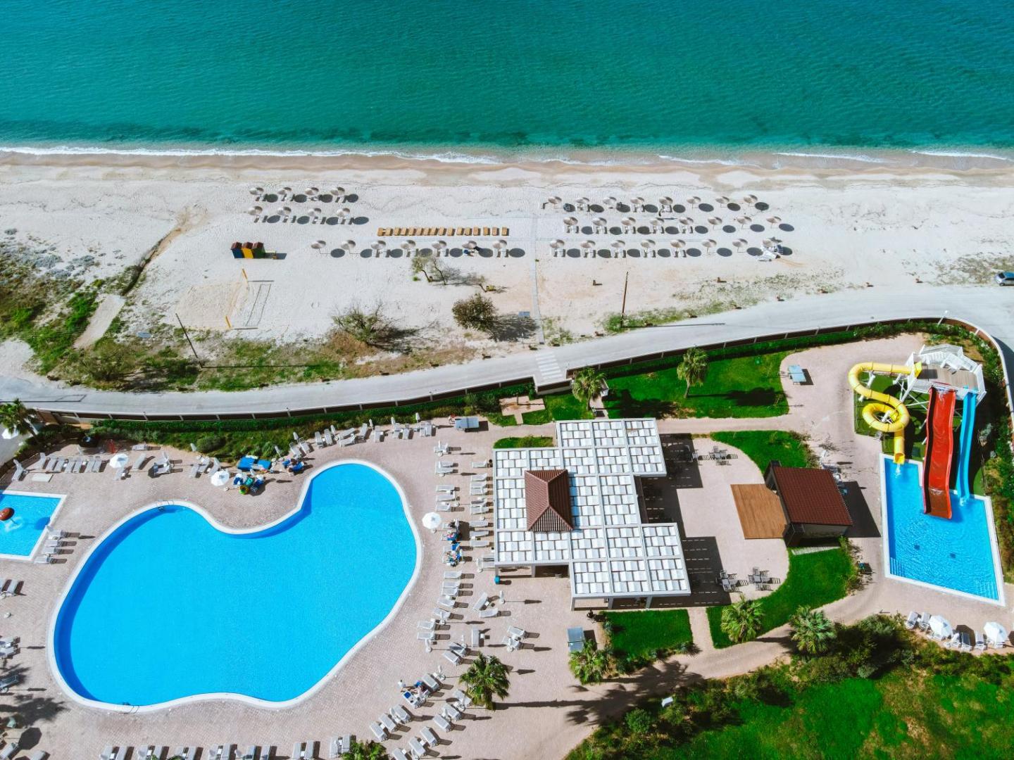 Almyros Beach Resort & Spa skats no augšas uz baseinu zonu, ūdens slidkalniņiem un smilšu pludmali pie dzidri zilās Jonijas jūras