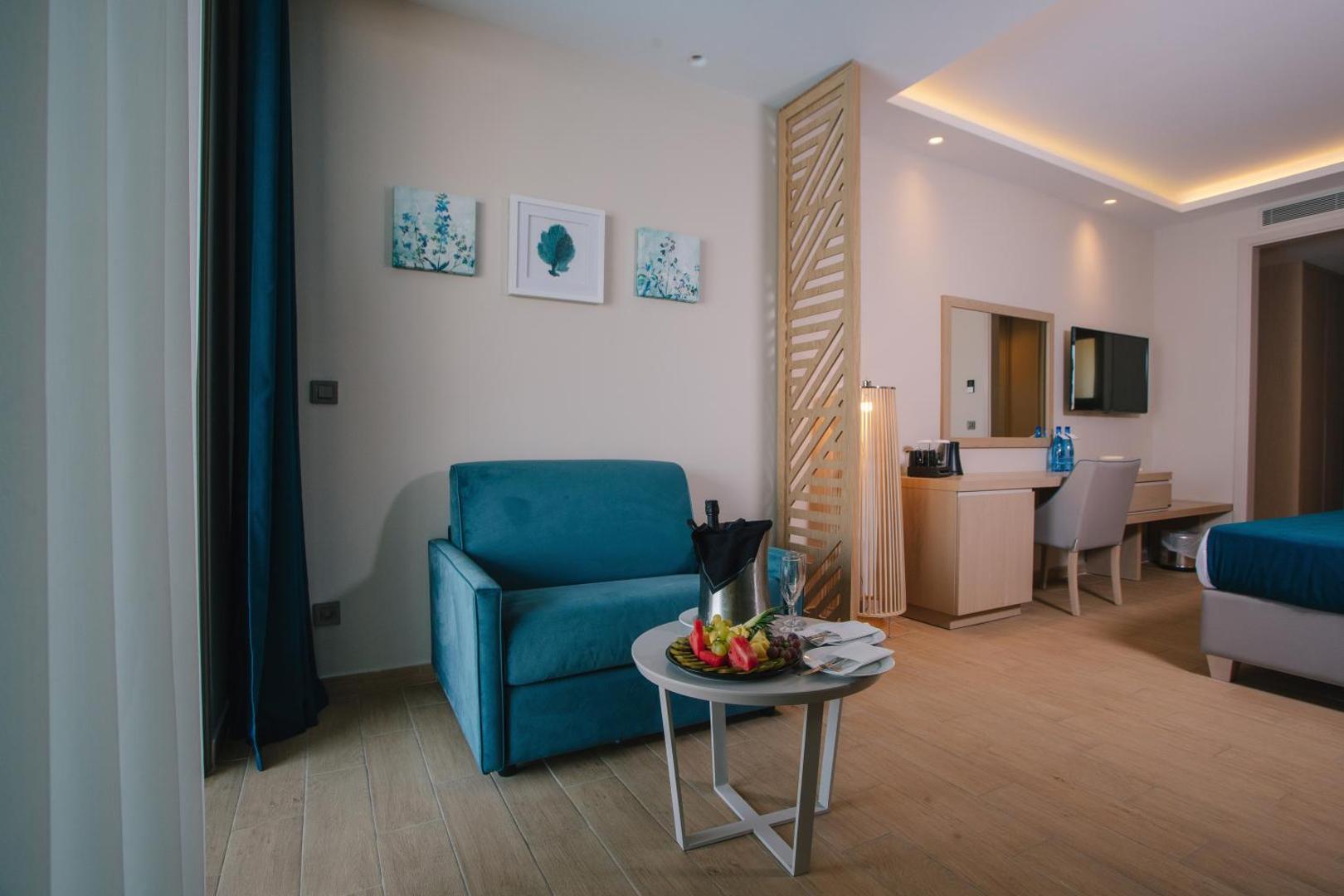 Almyros Beach Resort & Spa numura atpūtas zona ar zilu dīvānu, augļu plati un dzērieniem uz galda viesu sagaidīšanai