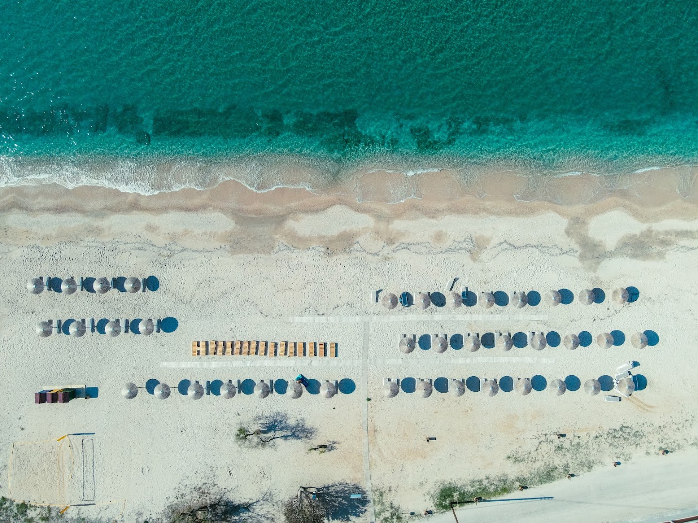 Almyros Beach Resort & Spa privātā pludmale no putna lidojuma — tirkīza ūdens, balti smilšu krasti un sakārtotas saulessargu rindas