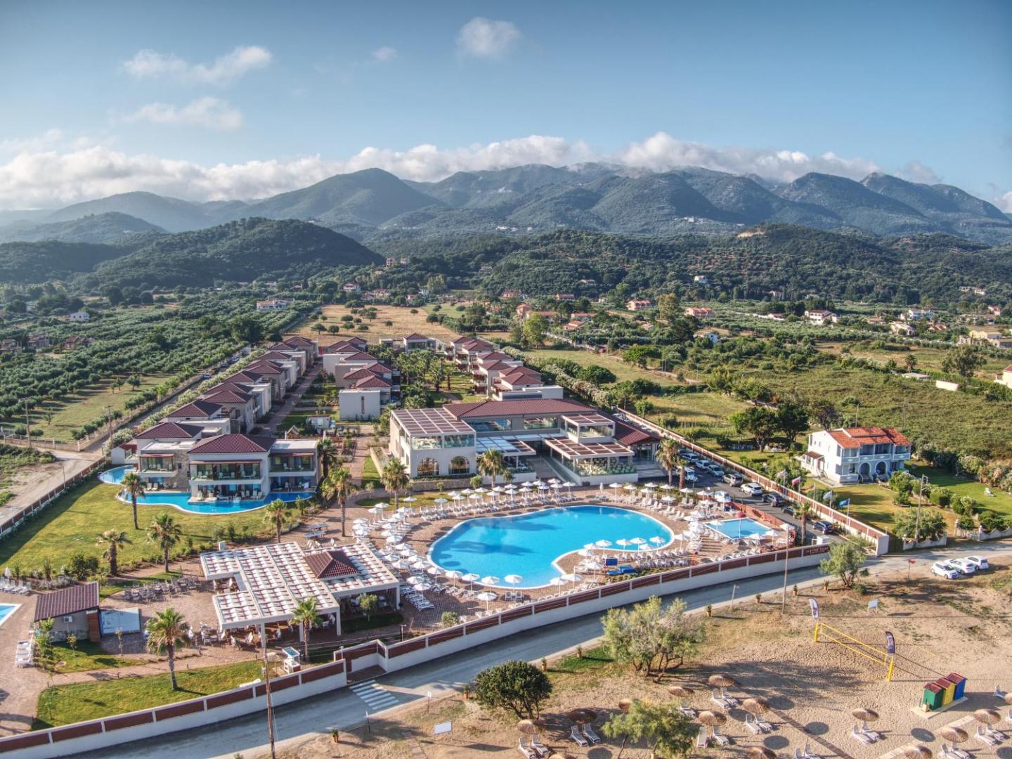 Almyros Beach Resort & Spa galvenais baseins ar sauļošanās krēsliem un viesnīcas korpusiem uz kalnu fona Korfu