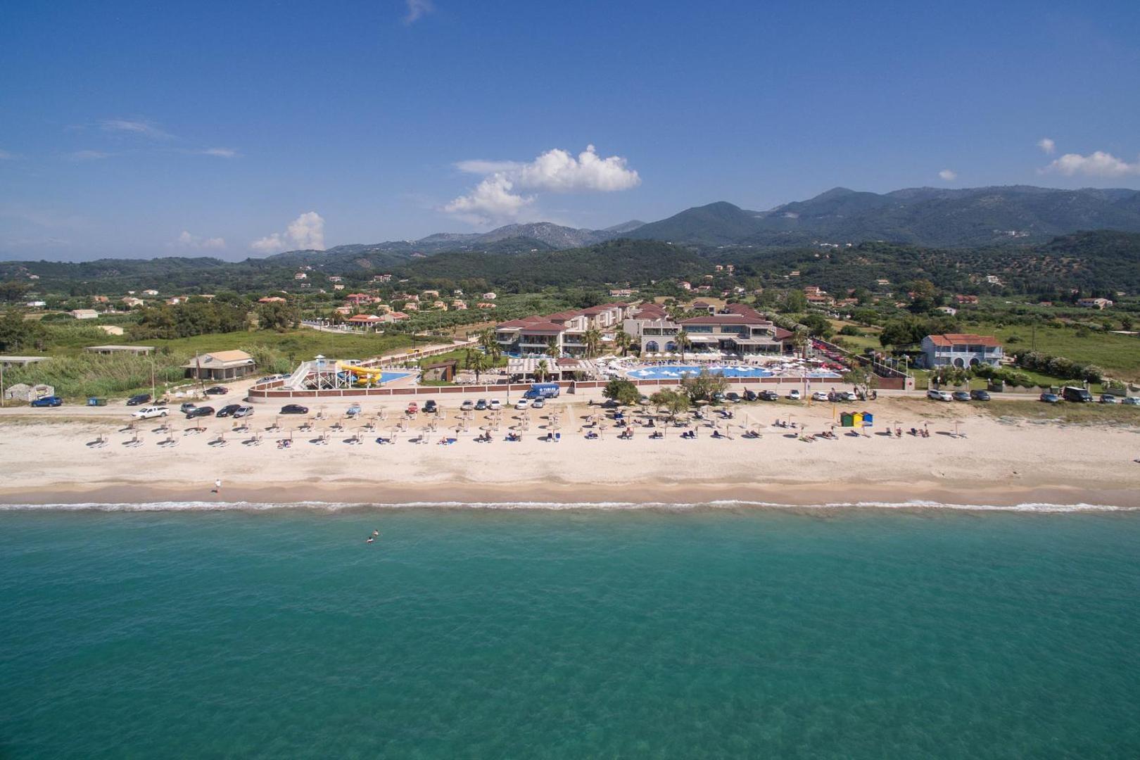 Almyros Beach Resort & Spa skats no jūras puses uz plašo smilšu pludmali un viesnīcas kompleksu saulainā dienā