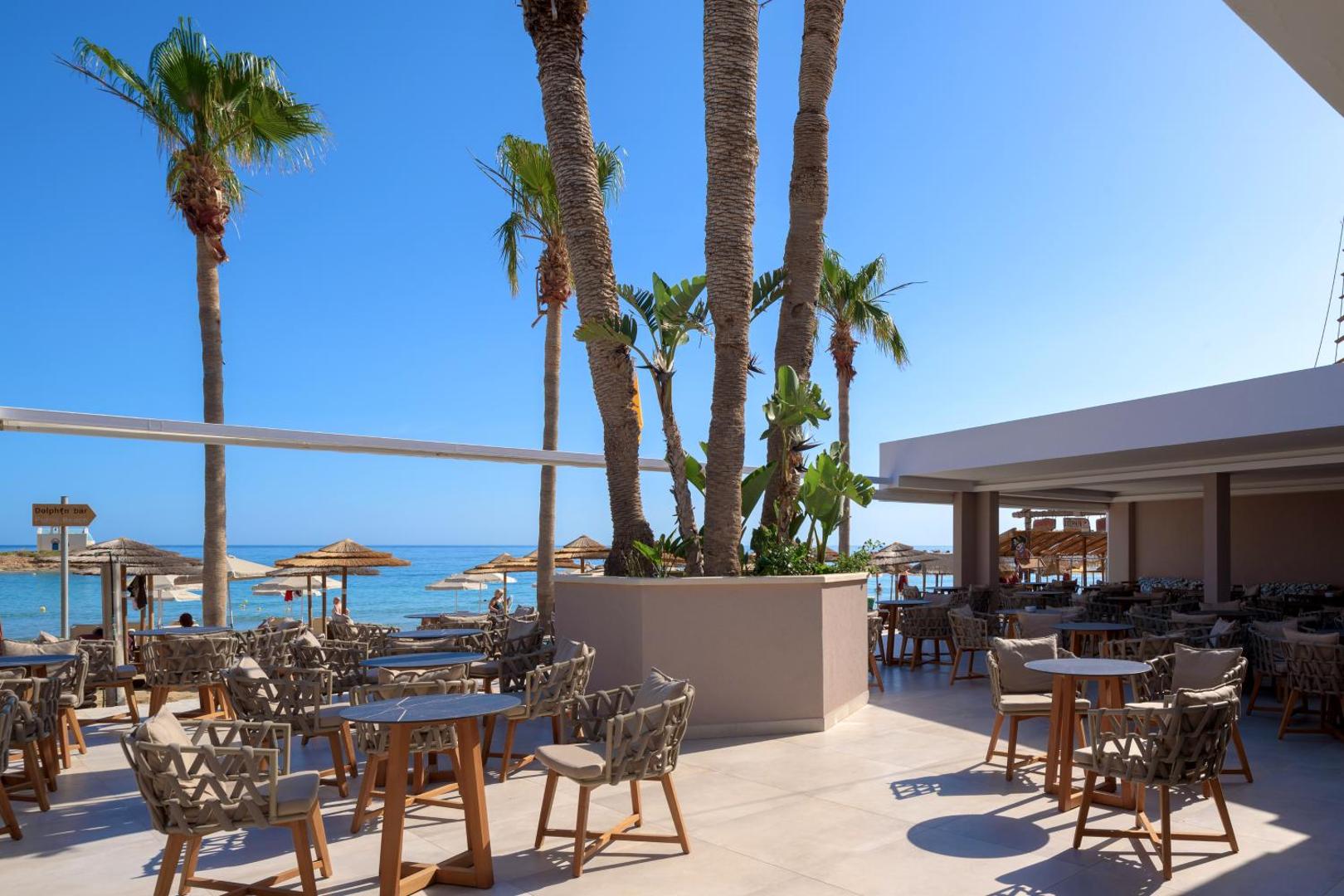 High Beach Resort atvērtā tipa restorāna terase ar skatu uz jūru Stalidā, Krētā — pīti krēsli, palmas un saulains pagalms