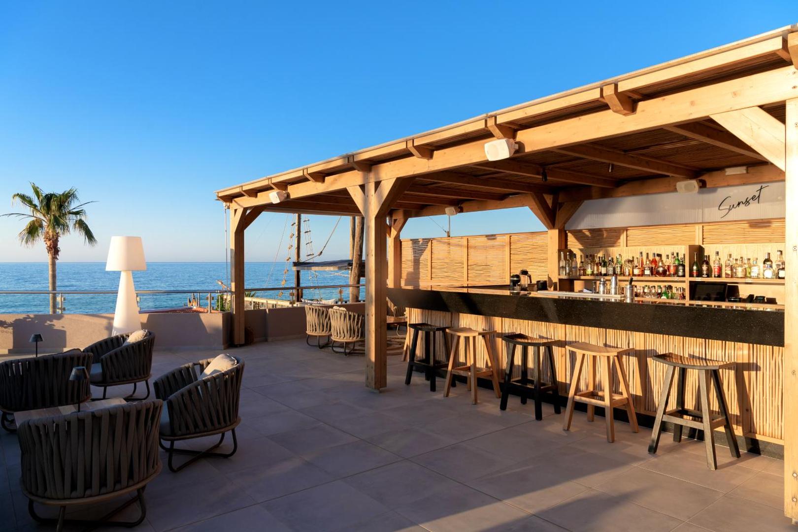 High Beach Resort bārs Sunset zelta stundā — koka konstrukcijas nojume, bāra lete ar dzērieniem un ērtiem atpūtas krēsliem