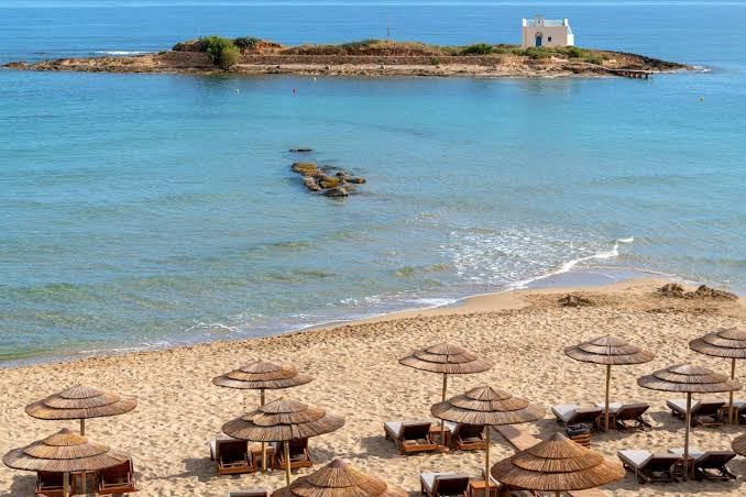 High Beach Resort privātā smilšu pludmale ar salmu saulessargiem un skatu uz nelielu salu ar baltu baznīcu jūrā
