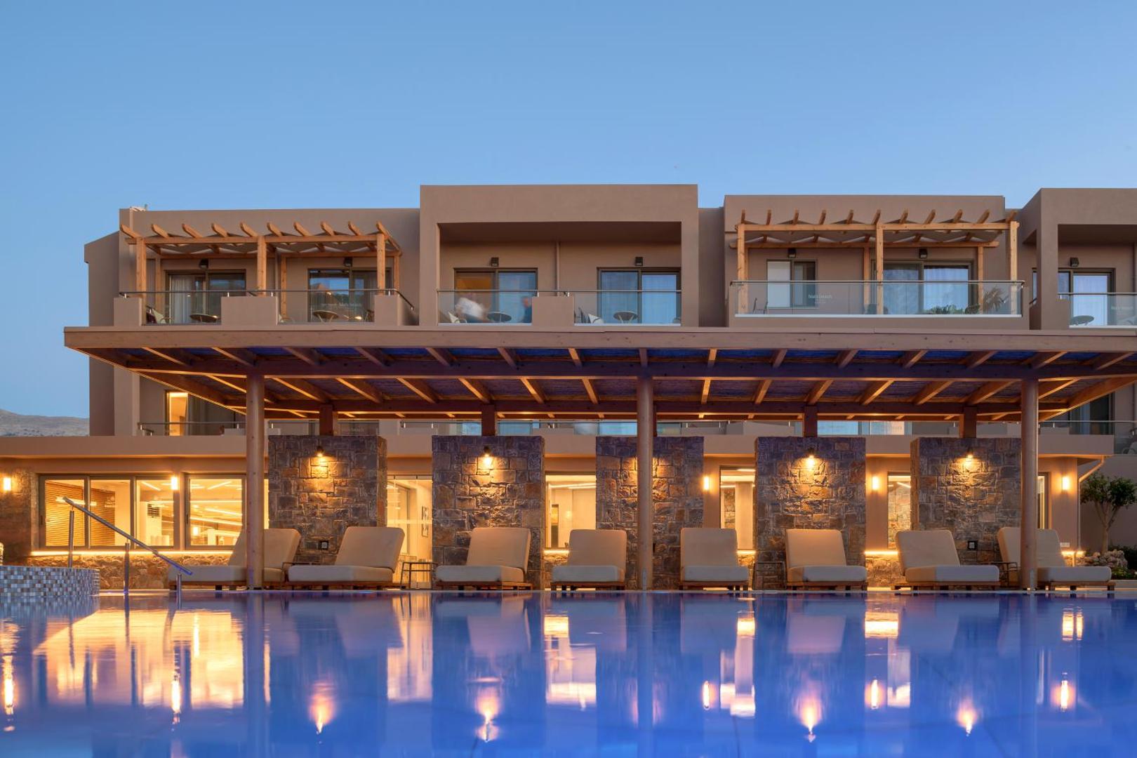 High Beach Resort vakara skats uz baseinu un viesnīcas fasādi ar izgaismotiem balkoniem Malijā, Krētā