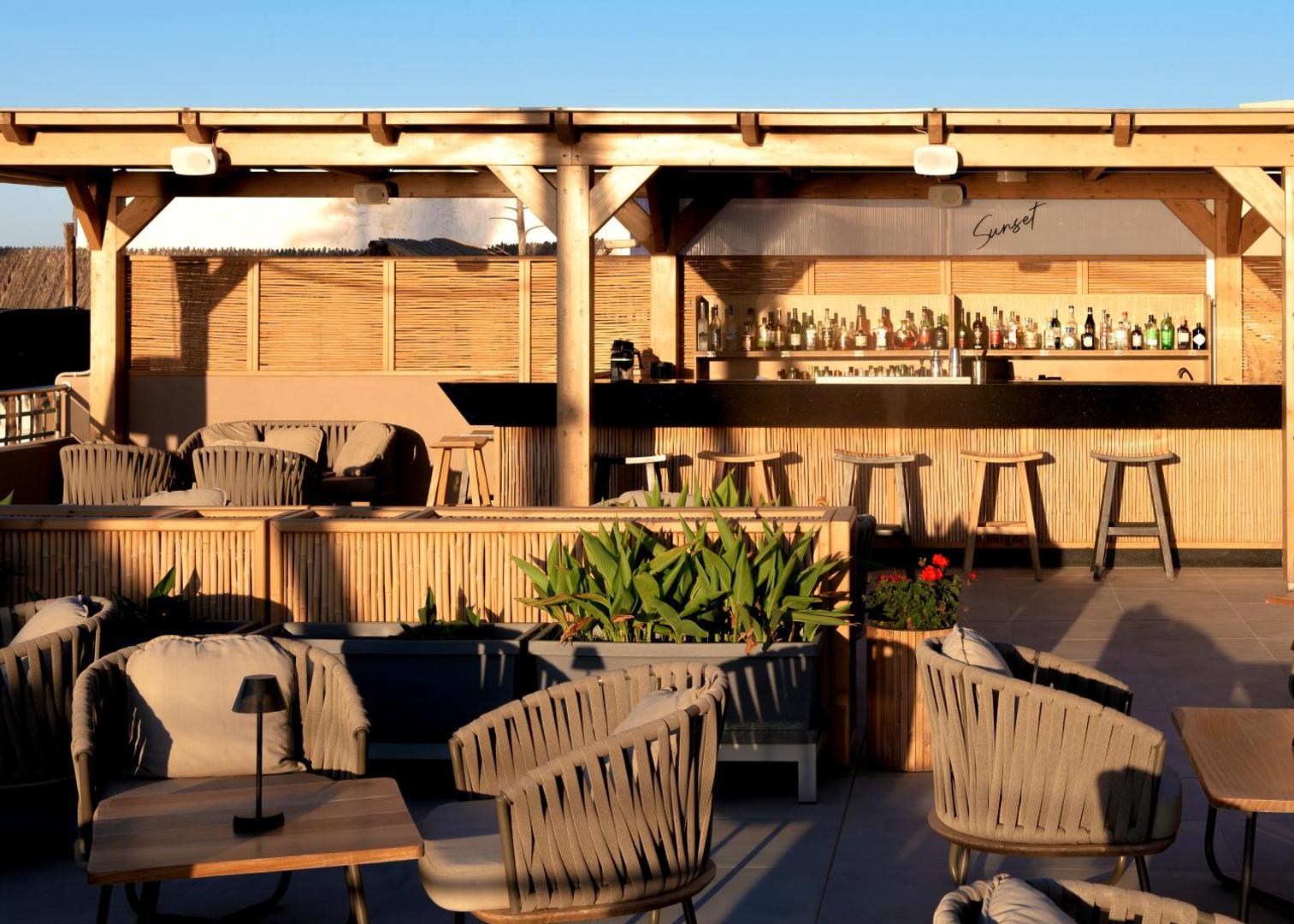High Beach Resort āra atpūtas zona ar stilīgiem krēsliem un galdiņiem pie Sunset bāra — mājīgs apgaismojums un koka apdare