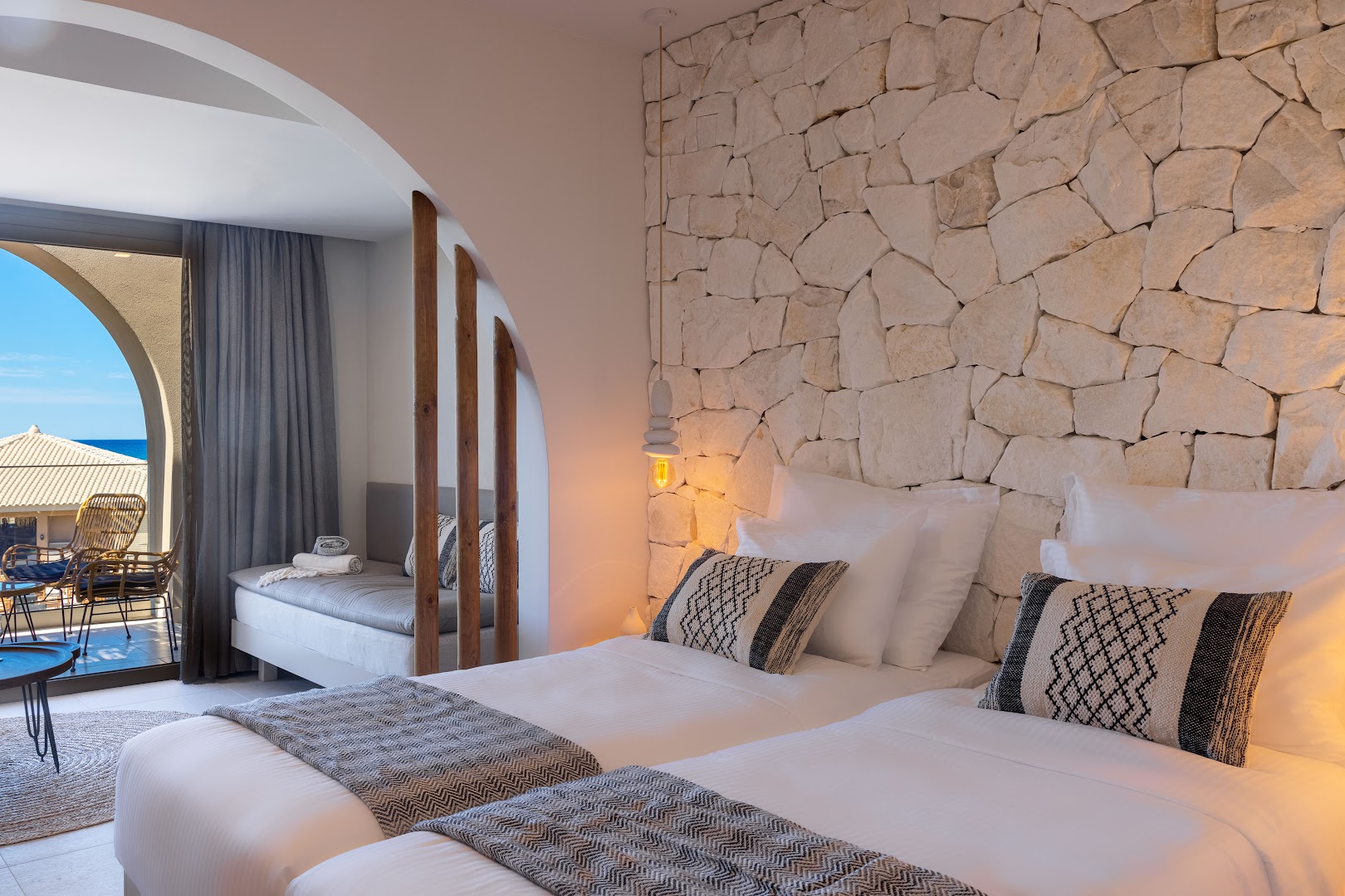 Eliros Mare Beachfront Poem Hotel numura interjers ar akmens sienu, mīkstiem spilveniem un skatu uz balkonu saulainā dienā