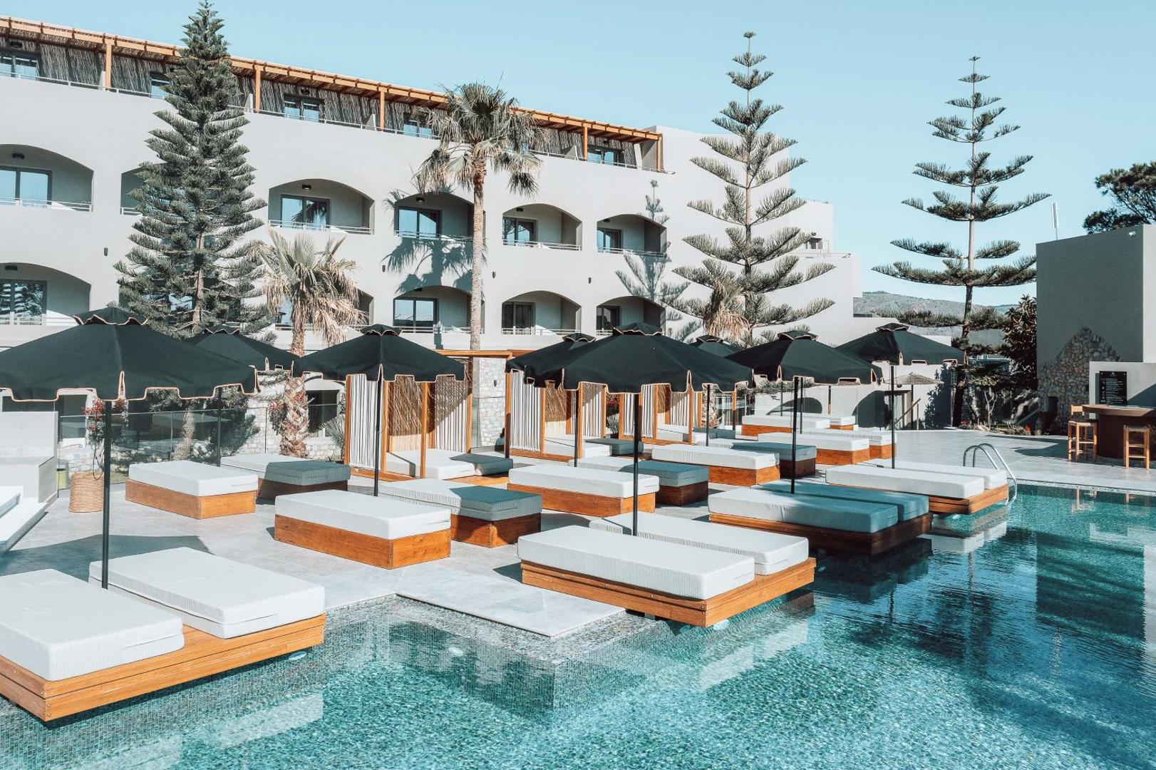 Eliros Mare Beachfront Poem Hotel ēkas fasāde ar balkoniem, priekšplānā baseins un rinda ar ērtiem atpūtas guļamkrēsliem
