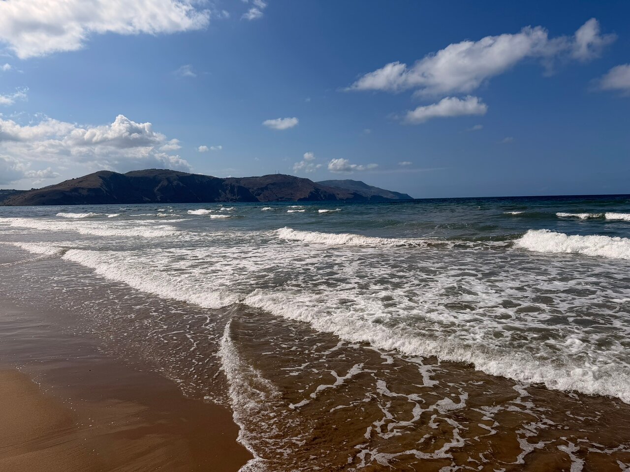 Eliros Mare Beachfront Poem Hotel pludmale Georgiupoli, Krētā — skats uz zilajiem jūras viļņiem un kalnu siluetu pie horizonta