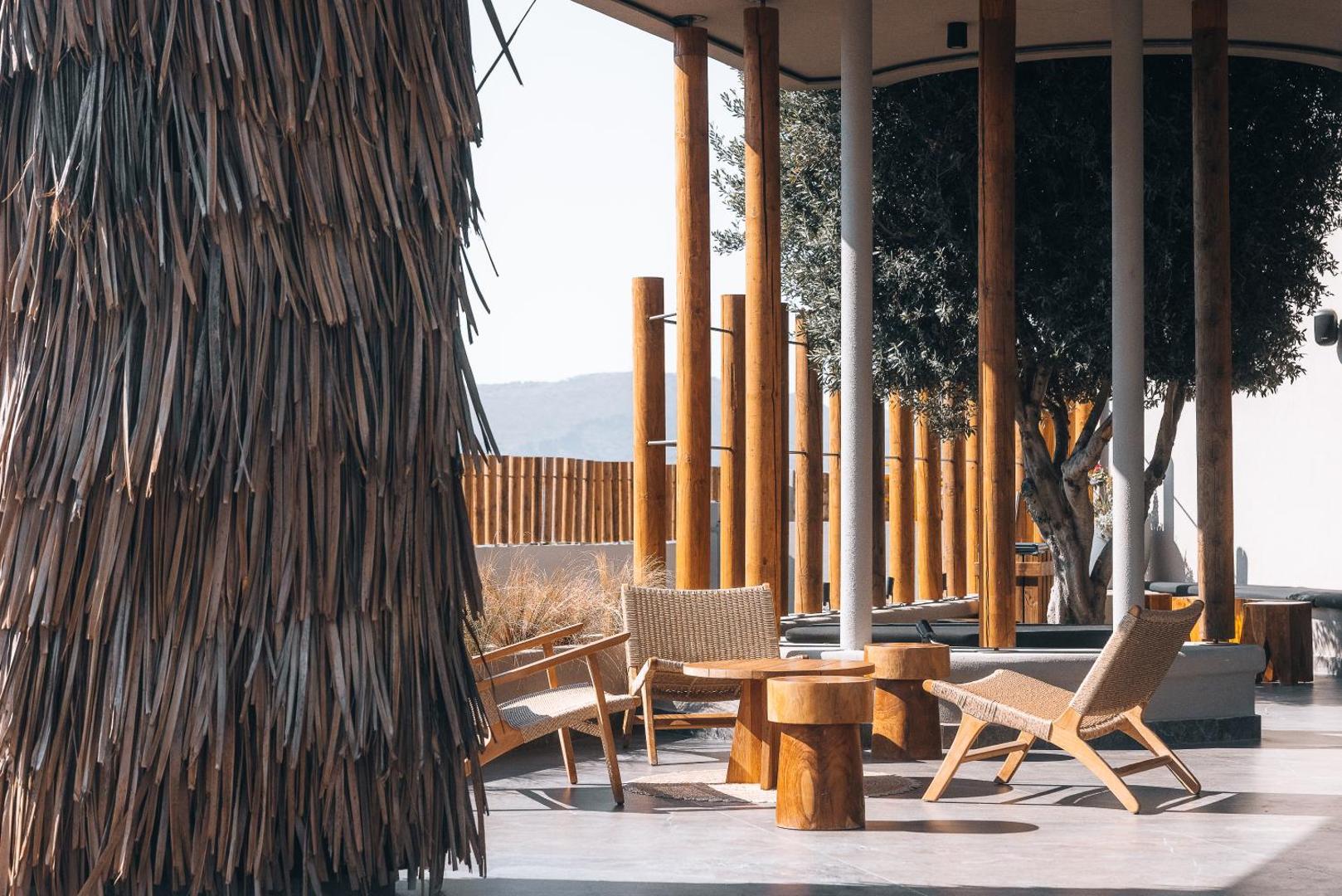 Eliros Mare Beachfront Poem Hotel āra atpūtas zona ar pītiem krēsliem un koka galdiņiem zem stilīgas nojumes