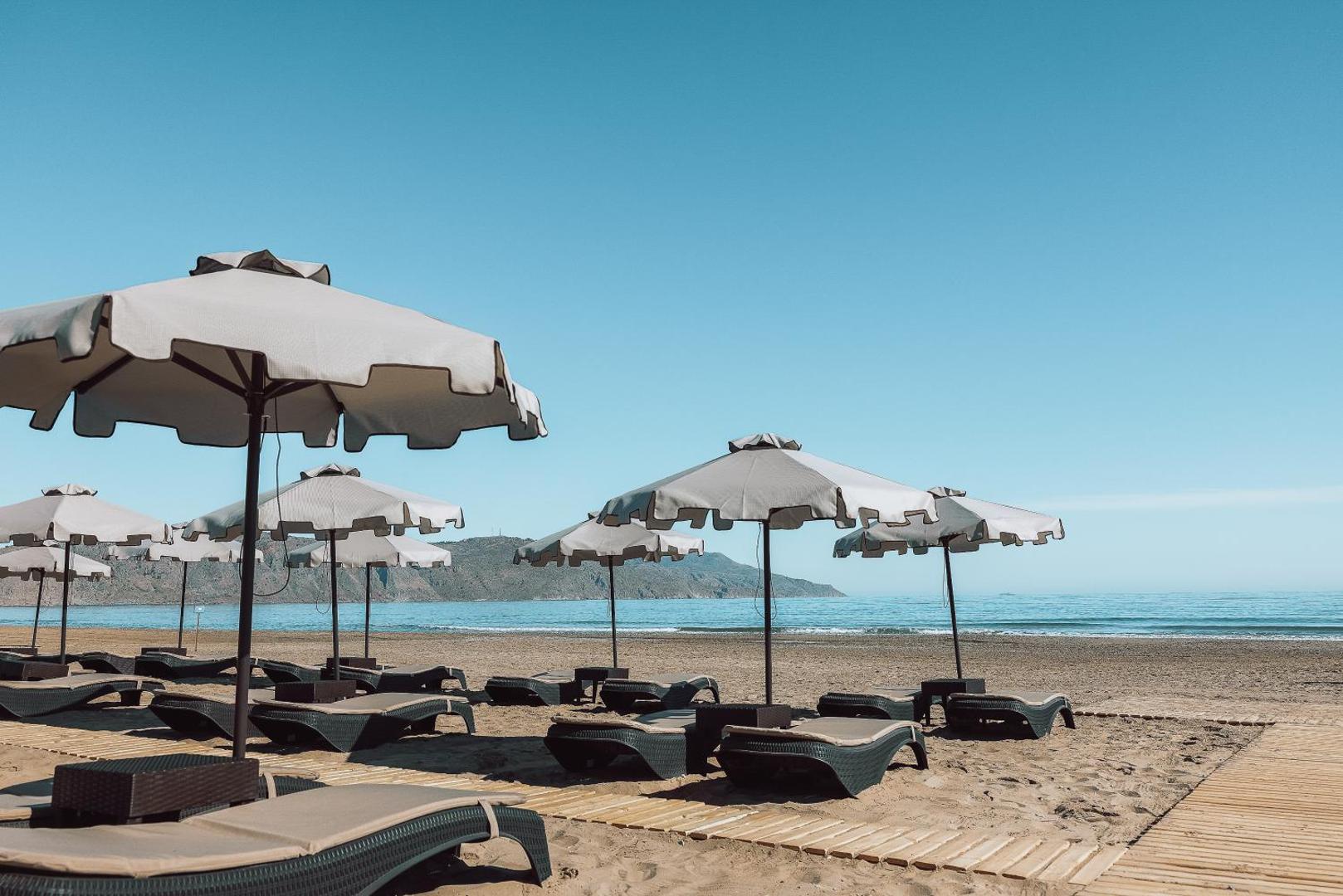 Eliros Mare Beachfront Poem Hotel pludmales atpūtas zona ar moderniem saulessargiem un ērtiem zviļņiem uz koka celiņiem