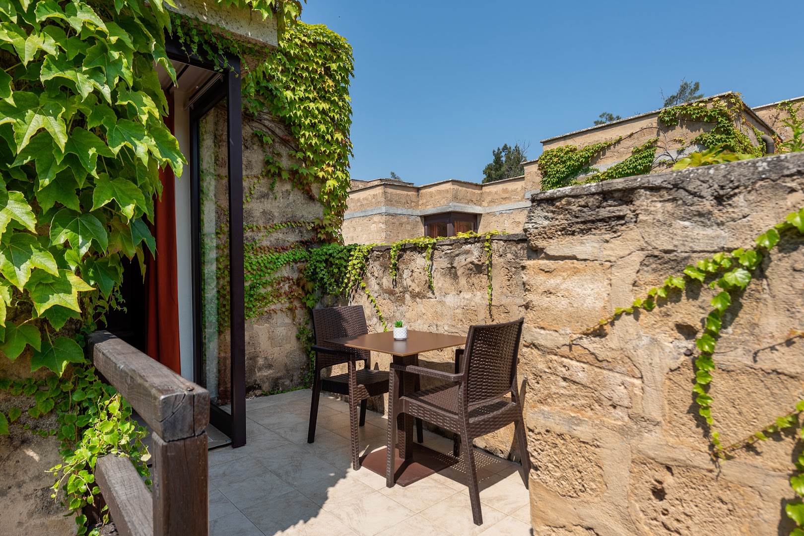 VOI Floriana Resort numura privātā terase ar pītiem krēsliem, galdiņu un akmens mūri, ko klāj zaļi vīteņaugi.