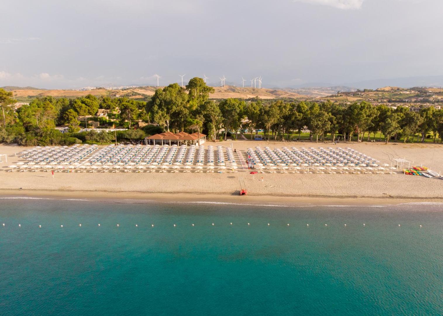 VOI Floriana Resort panorāmas skats uz viesnīcas kompleksu, pludmales bāru un apkārtnes pakalniem ar vēja ģeneratoriem