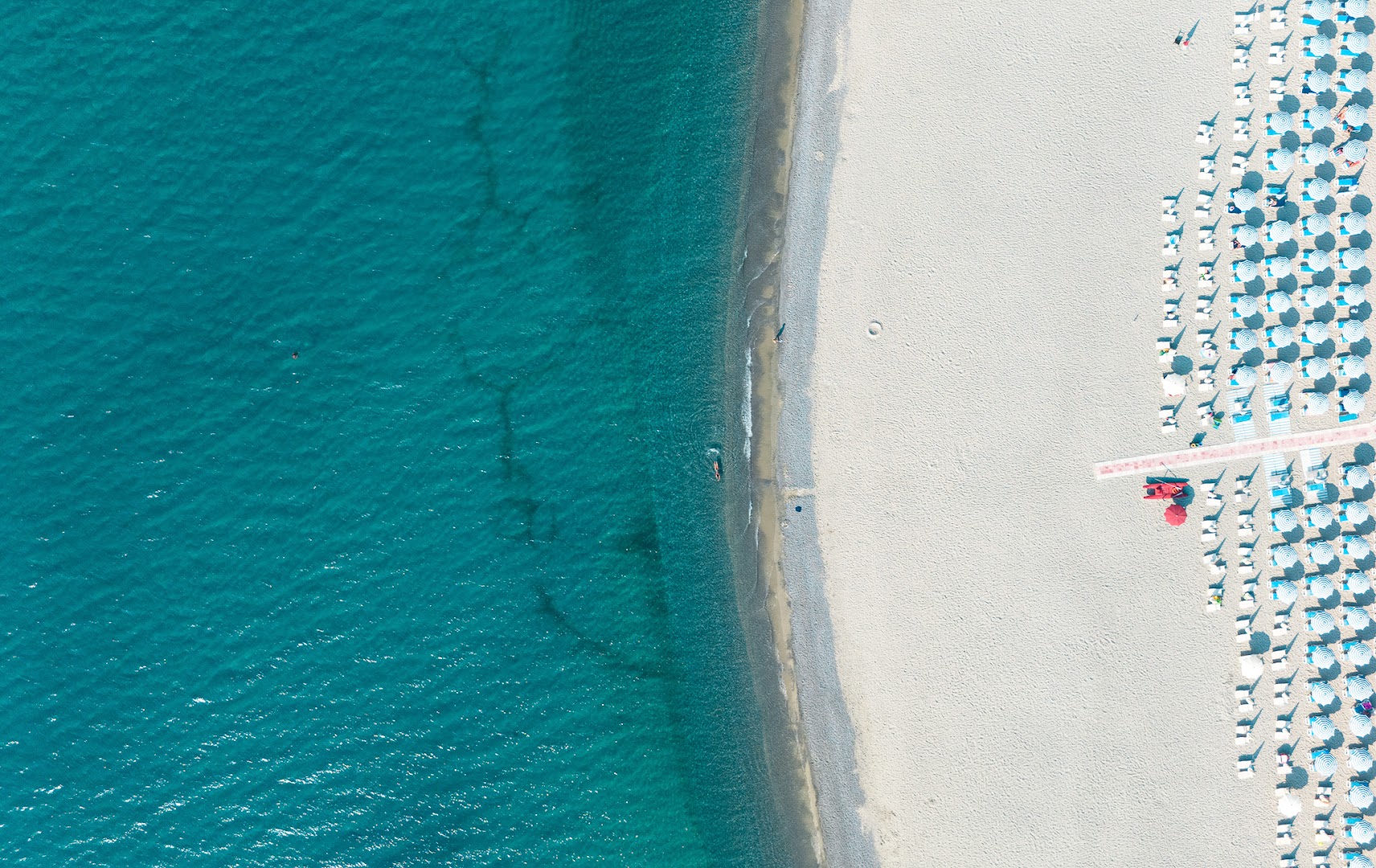 VOI Floriana Resort skats no augšas uz dzidri zilo Jonijas jūru un balto smilšu pludmali ar saulessargiem Kalabrijā