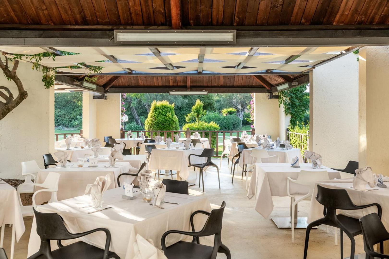 VOI Floriana Resort restorāna āra terase ar klātiem galdiem zem koka nojumes un skatu uz dārzu
