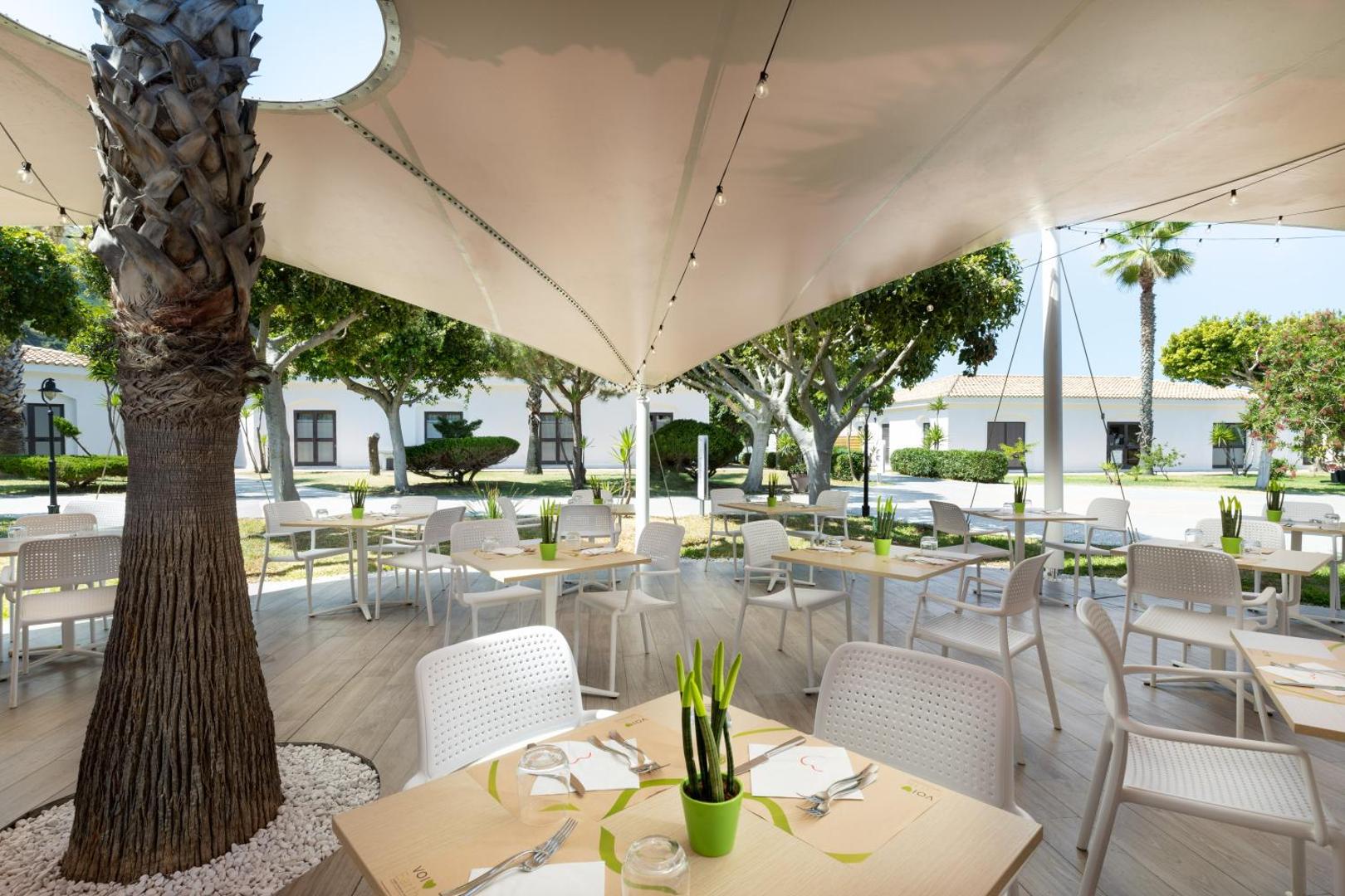 VOI Le Muse Essentia restorāna āra terase zem saules buras ar skatu uz viesnīcas dārzu un bungalo