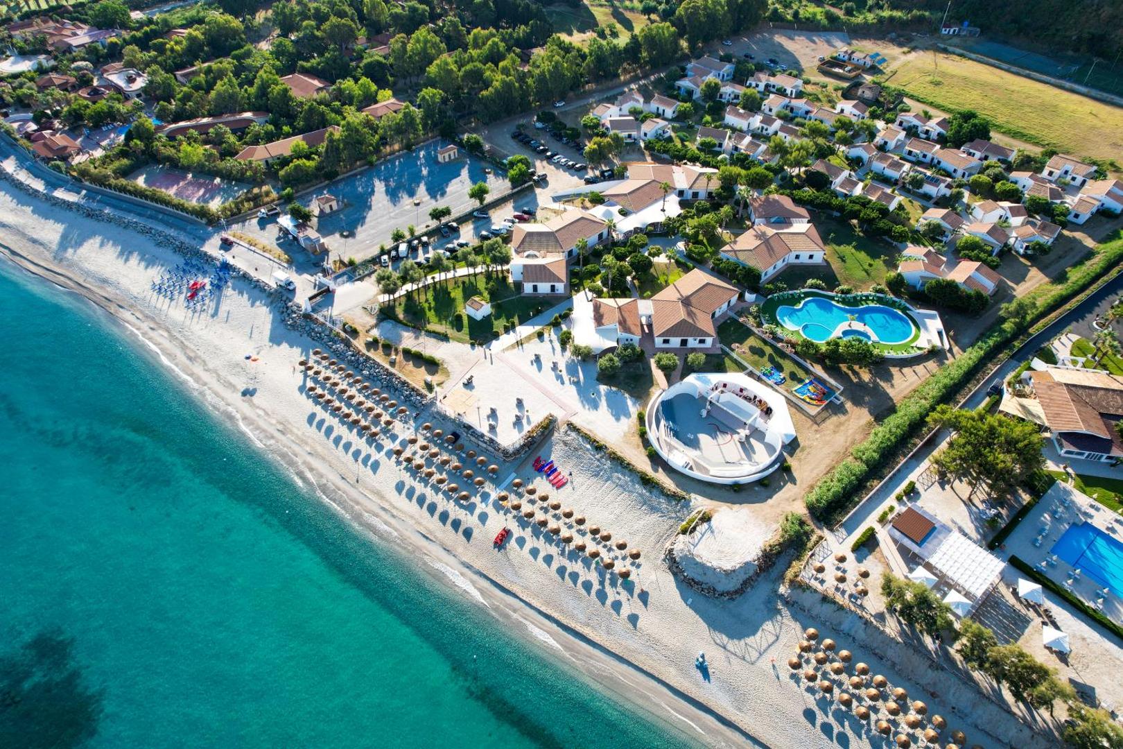 VOI Le Muse Essentia aerofoto ar baseinu, brīvdabas skatuvi un piekrastes joslu — plaša zaļā teritorija Kalabrijā