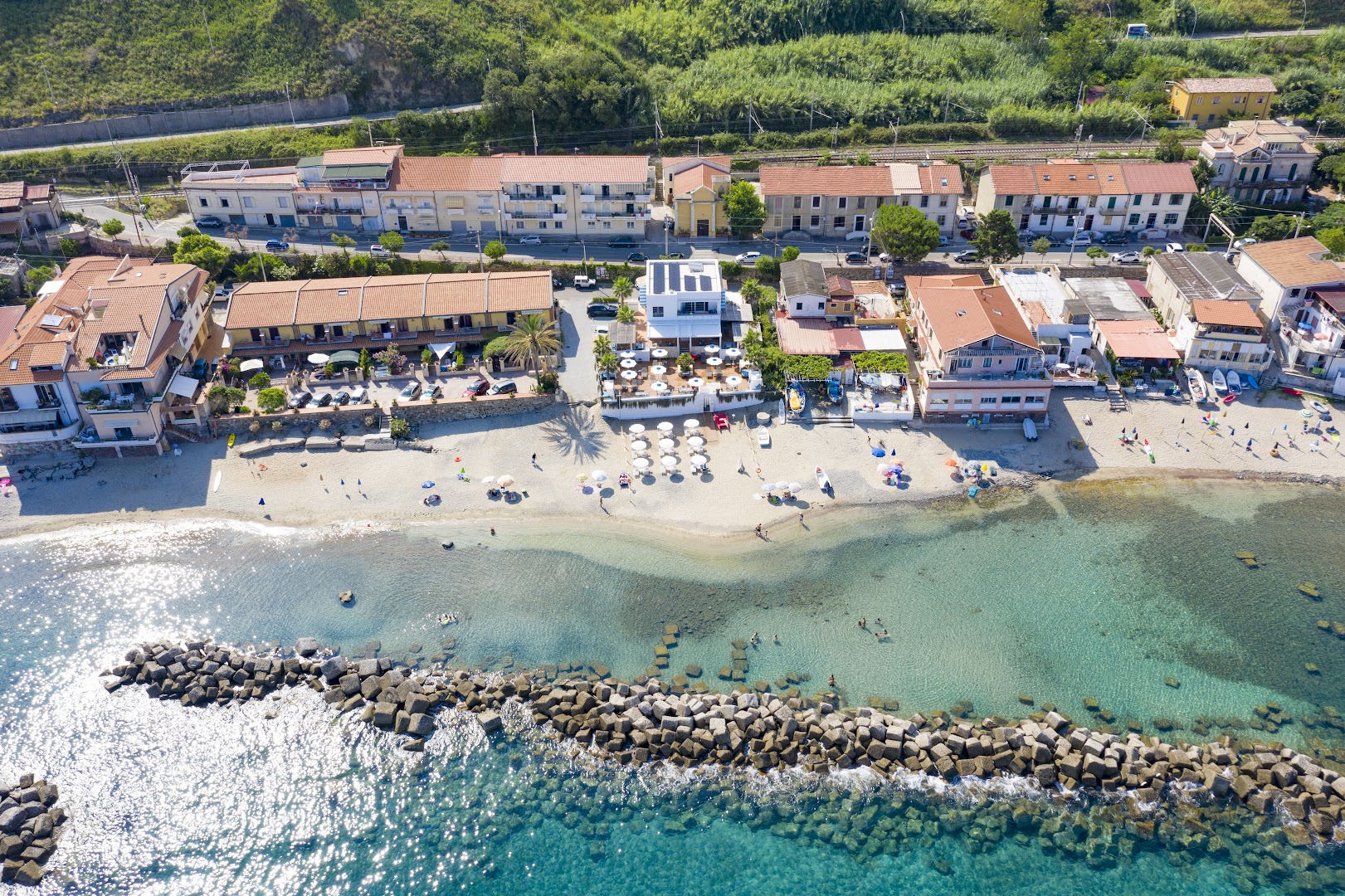 Piccolo Grand Hotel skats no putna lidojuma Kalabrijas piekrastē — viesnīcas ēkas pie smilšu pludmales un dzidra tirkīza ūdens