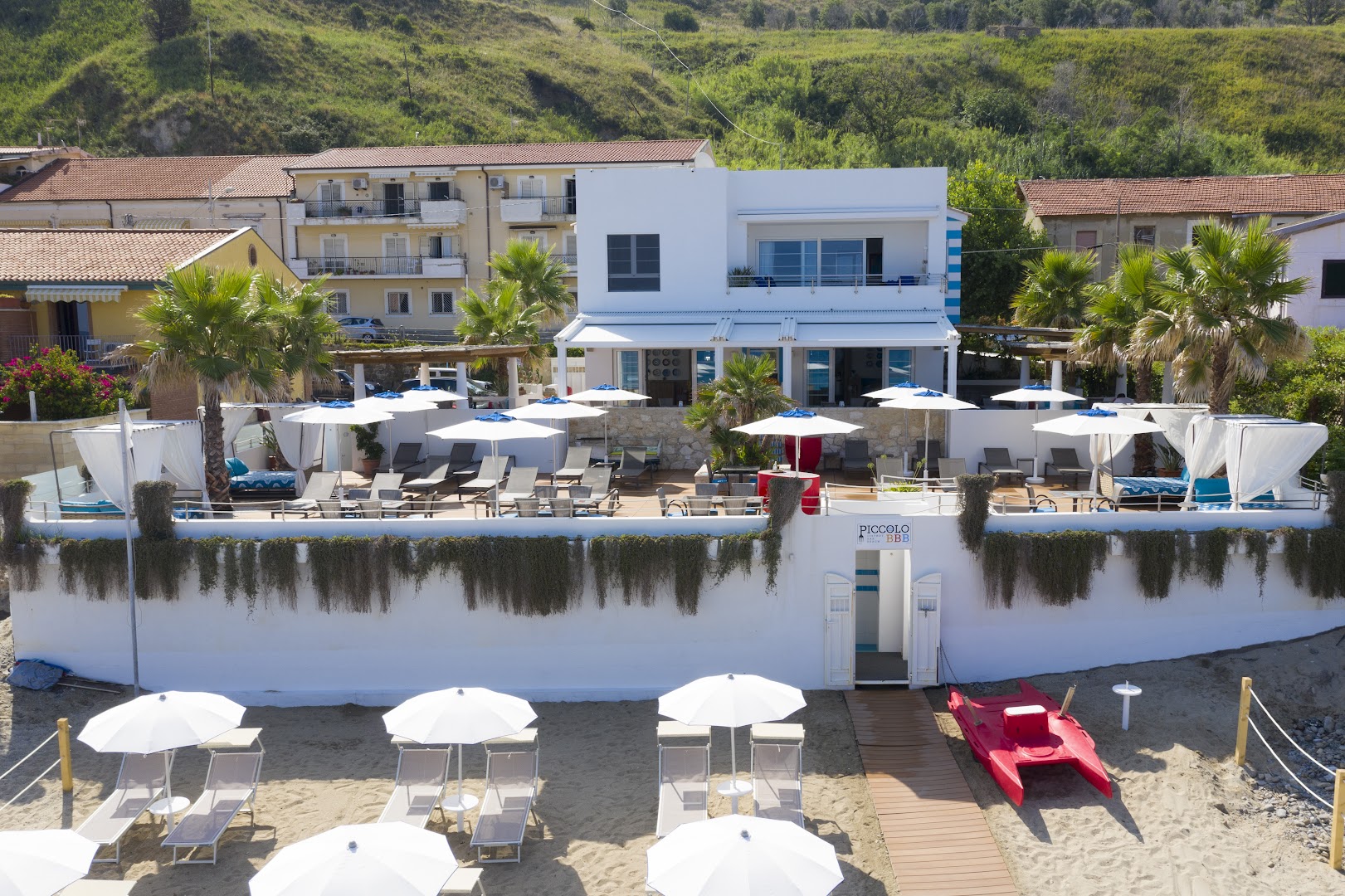 Piccolo Grand Hotel pludmales klubs ar baltiem saulessargiem, gultām un ieeju tieši no smilšu pludmales