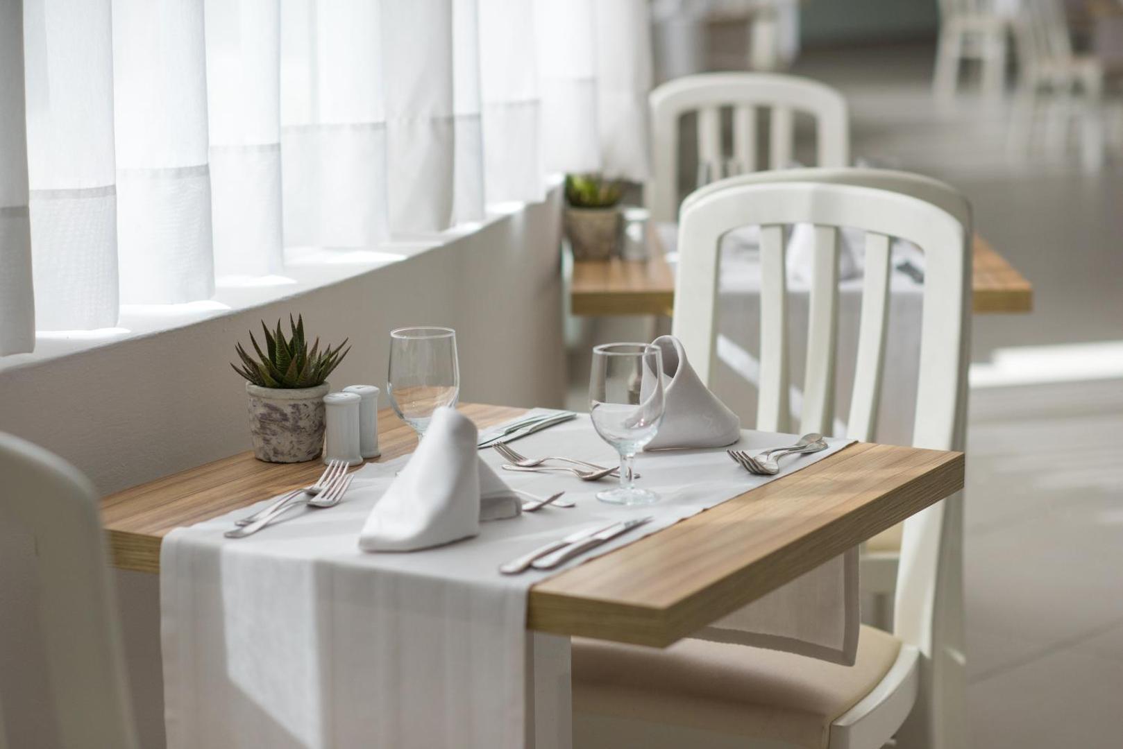 Iberostar Waves Bouganville Playa restorāna galda klājums ar baltu galdautu, galda piederumiem un dekoratīvu augu pie loga