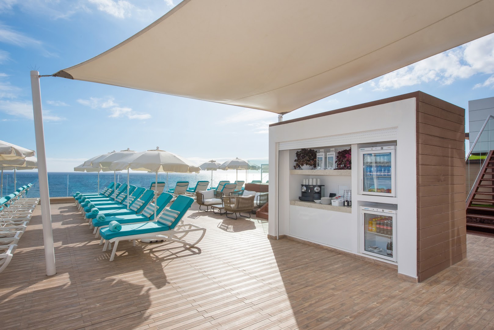 Iberostar Waves Bouganville Playa sauļošanās terase ar tirkīza krēsliem, saulessargiem un pašapkalpošanās bāru pie okeāna Tenerifē