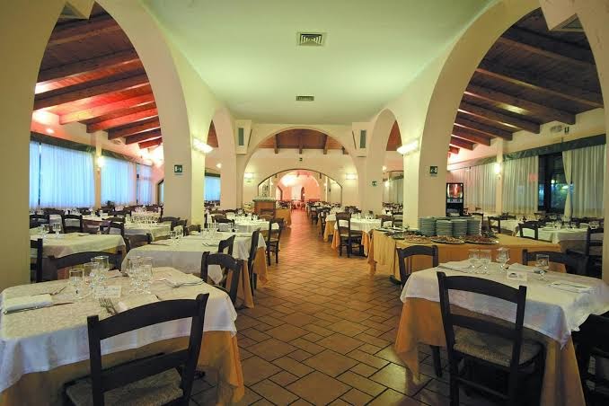 Th Le Castella Baia Degli Dei Village galvenais restorāns ar arkveida griestiem, flīžu grīdu un klātiem galdiem vakariņām