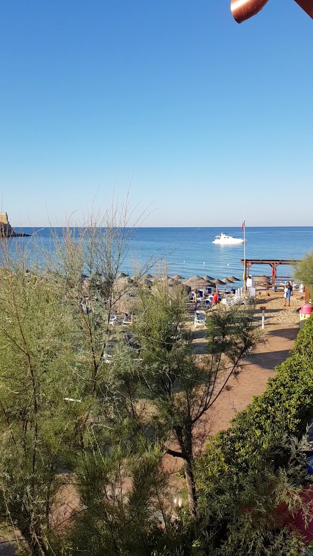 Skats uz Th Le Castella Baia Degli Dei Village privāto pludmali Kalabrijā ar saulessargiem, smiltīm un jahtu jūrā