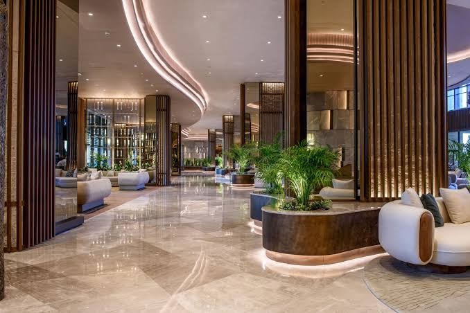 Viesnīcas Regnum The Crown lobby zona ar marmora grīdām, elegantiem dīvāniem un telpaugiem mūsdienīgā interjerā