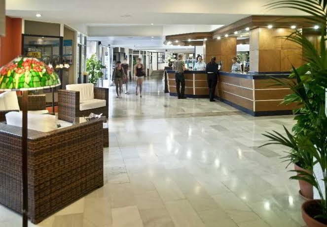 Hovima Santa Maria viesnīcas plašā recepcijas zona un vestibils Tenerifē ar atpūtas krēsliem un reģistrācijas leti gaišos toņos